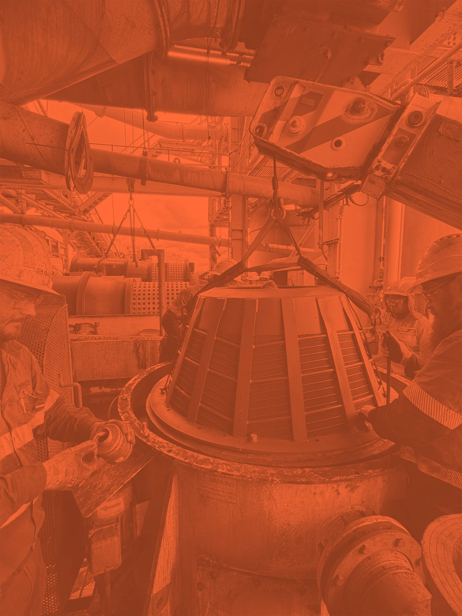 Industrial workers handling large machinery in a factory setting with pipes and equipment.