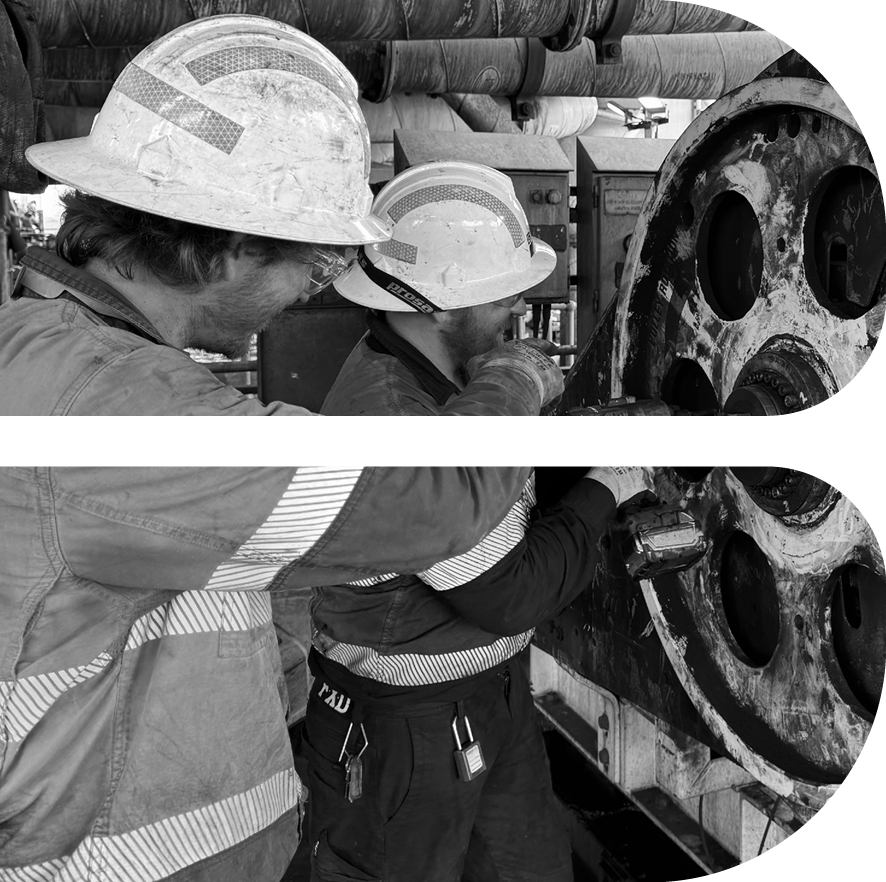 Two workers wearing hard hats and protective gear operate machinery, focusing on large gears in an industrial setting.