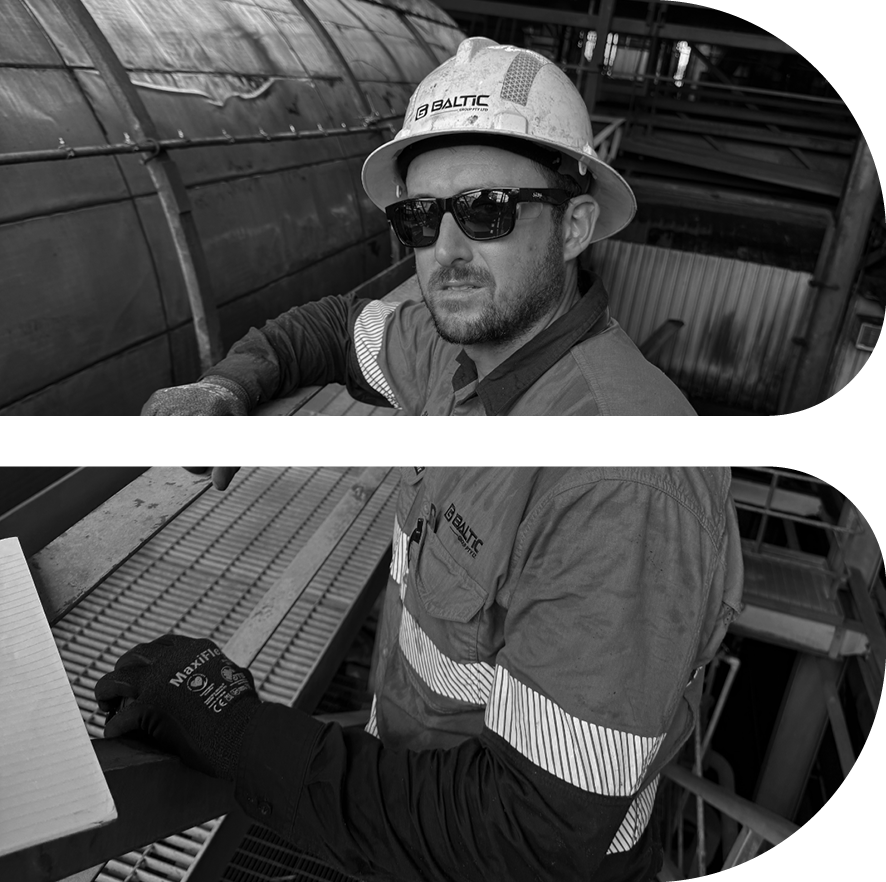 Black and white image of a male worker wearing a hard hat and safety glasses at an industrial site.