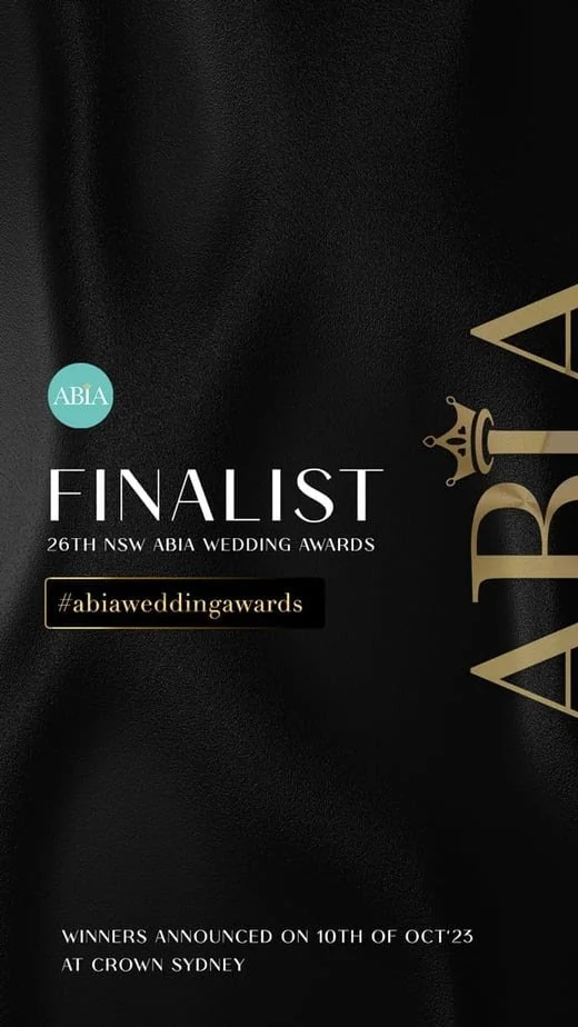 The image announces a finalist at the 26th NSW ABIA Wedding Awards, with winners to be announced on October 10, 2023, at Crown Sydney. It includes hashtags #abiaweddingawards and features a black and gold design with a crown graphic.