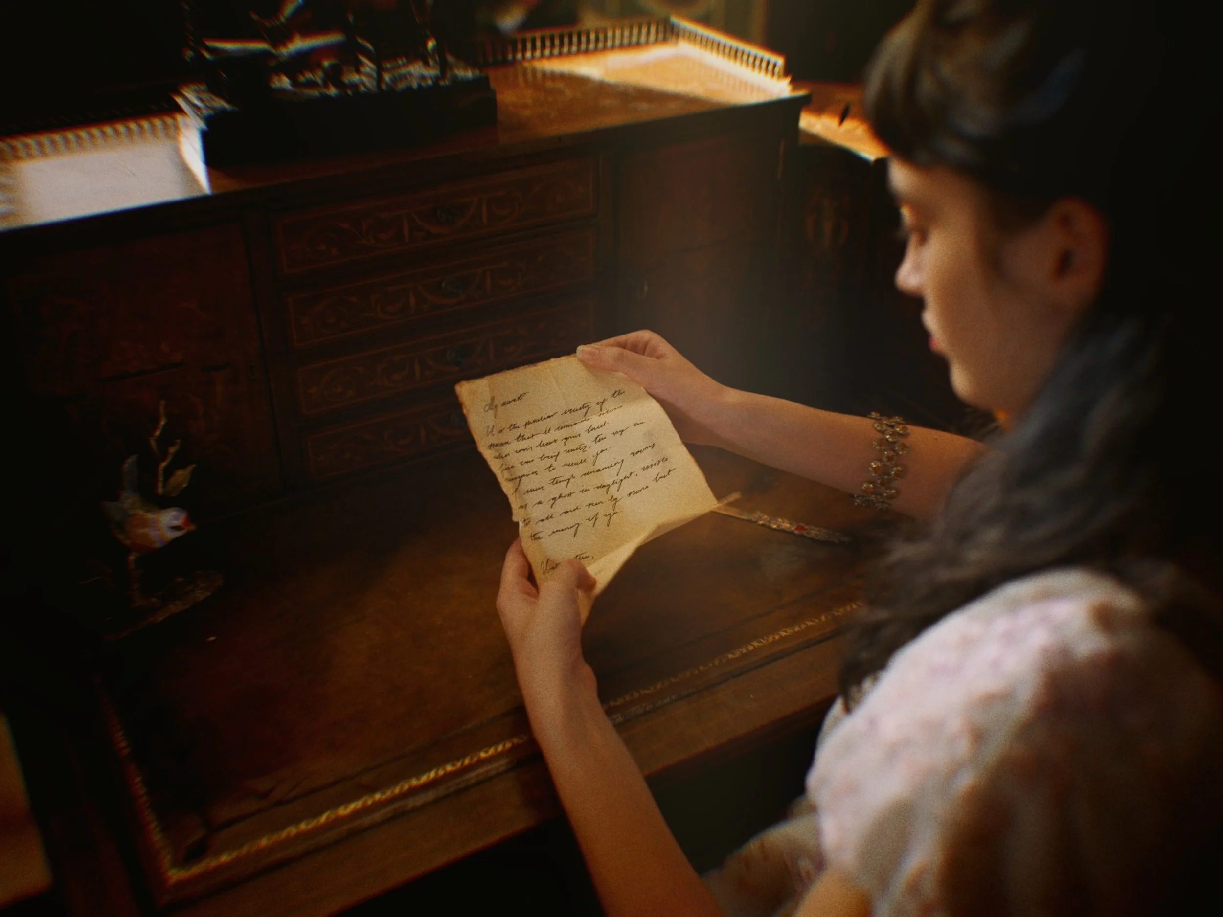 A woman in a white dress sits at her desk and reads a hand-written note, The Secret Life of Props
