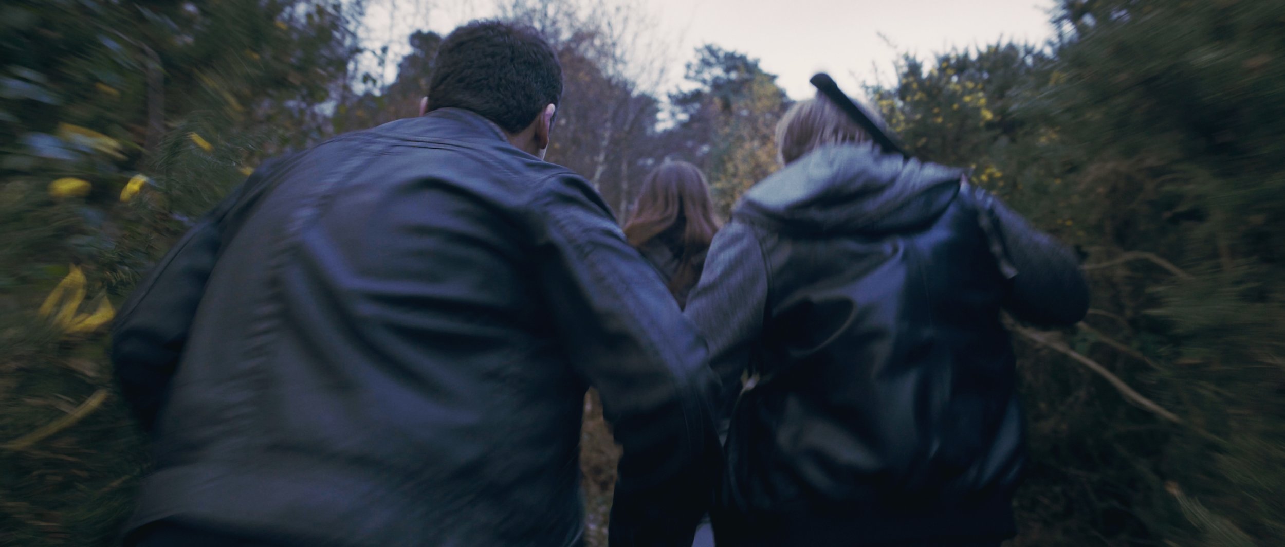 Three people in dark clothing holding weapons run through the forest, Flying Blind