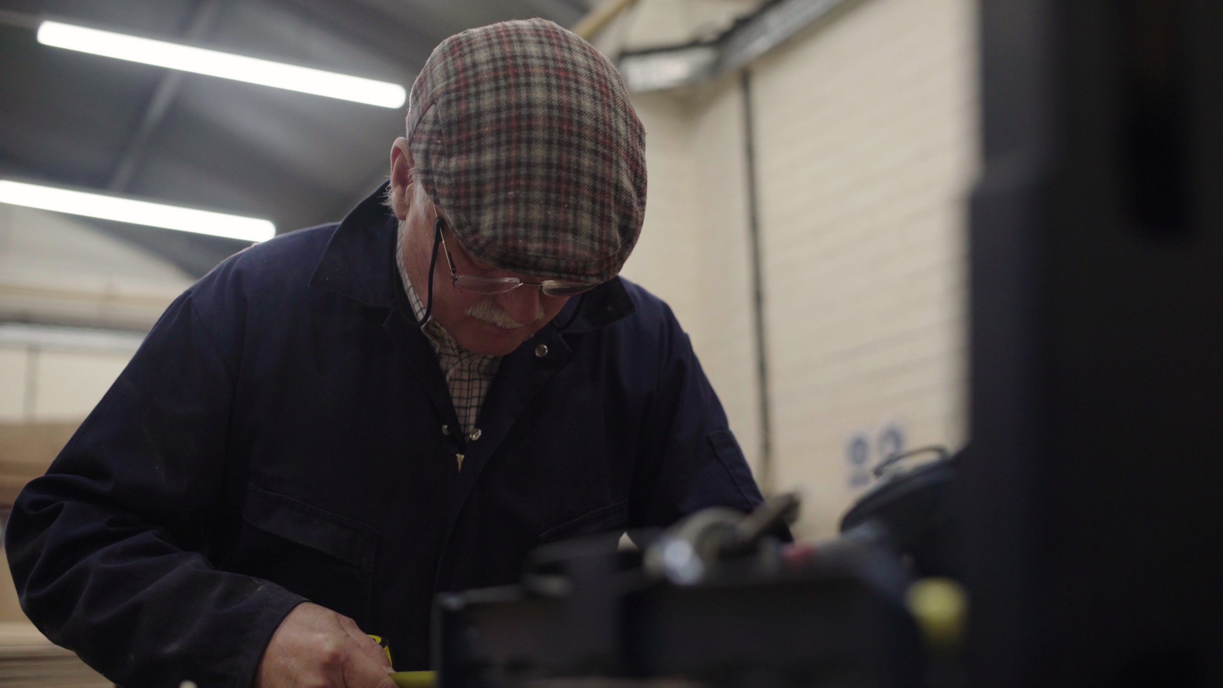 An elderly man in blue overalls works on a wood project, Men's Shed