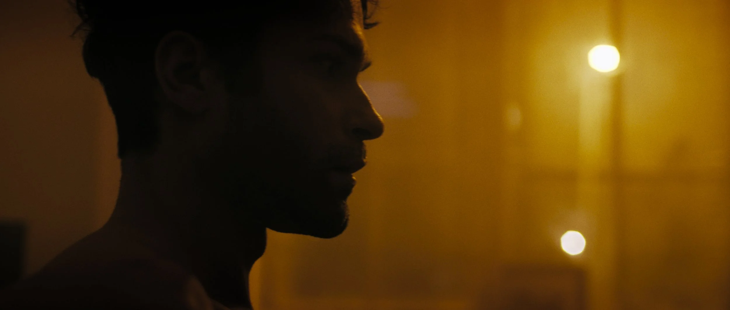 A man sits up in bed silhouetted against orange coloured streetlights, Night Whispers