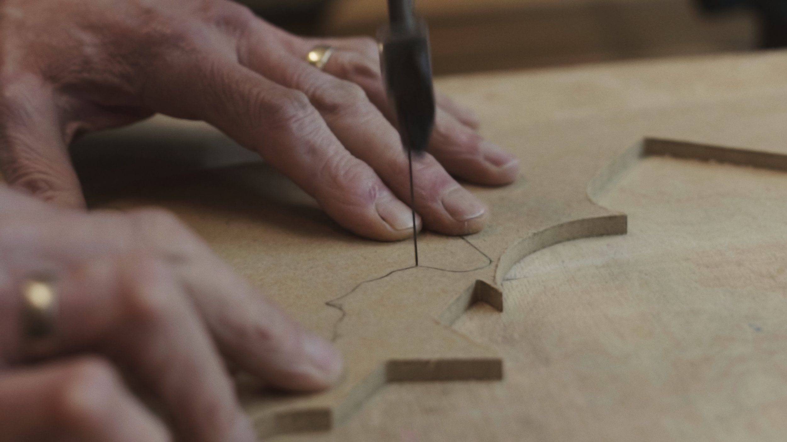 An elderly man's hands move a piece of wood to cut out a specific shape, The Last Toymaker