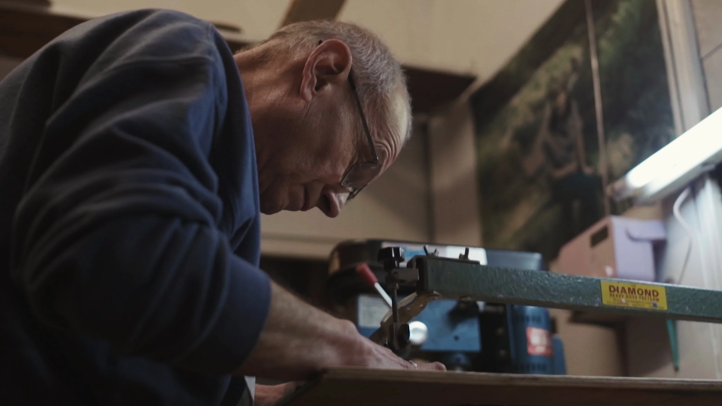 An elderly man works at his wood-cutting machine, The Last Toymaker