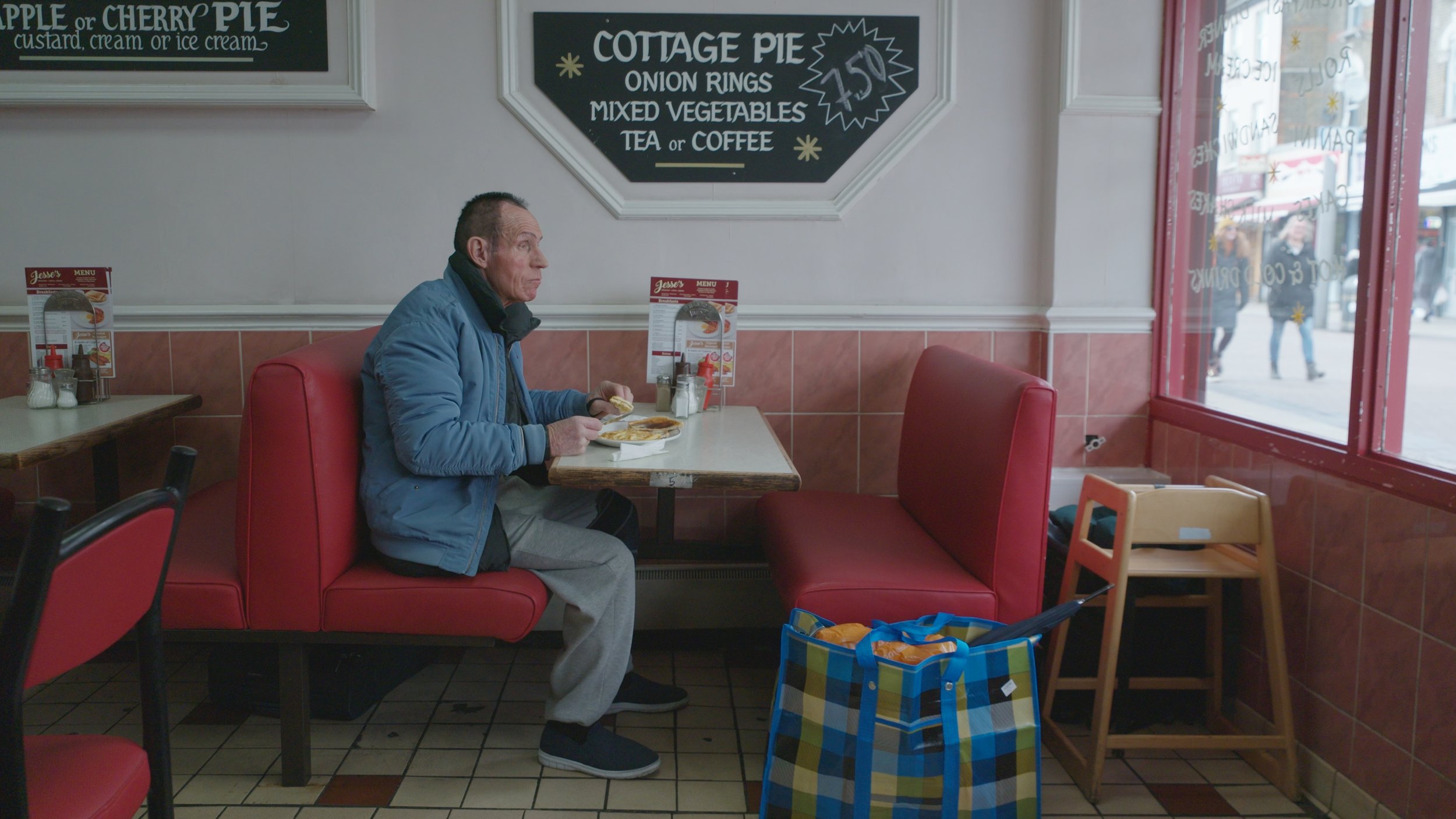 King Dick (Brian Jason) sits at a table in a café and eats food