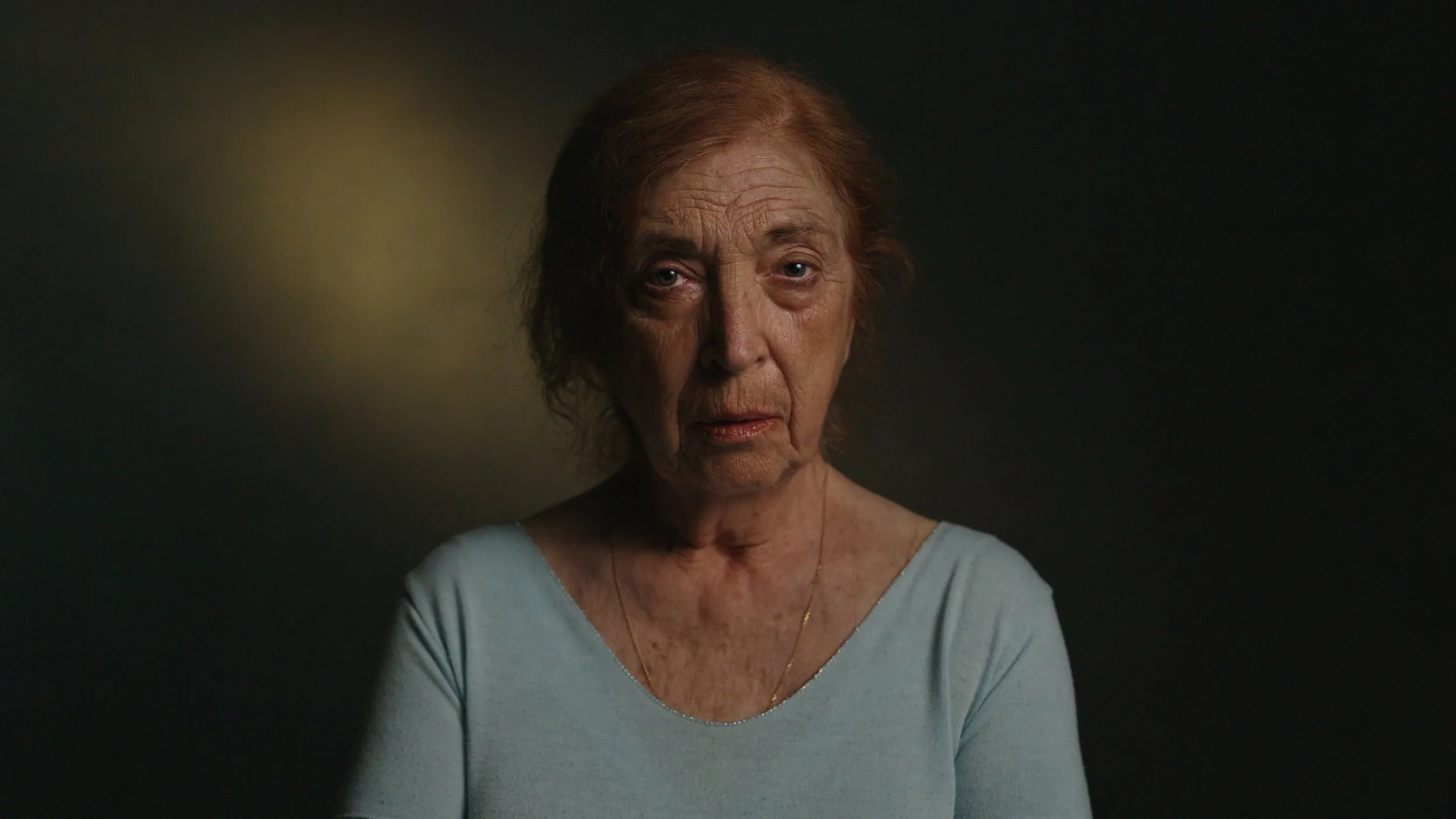 An elderly woman looks into camera in-front a dark backdrop, It's Not Just Banter