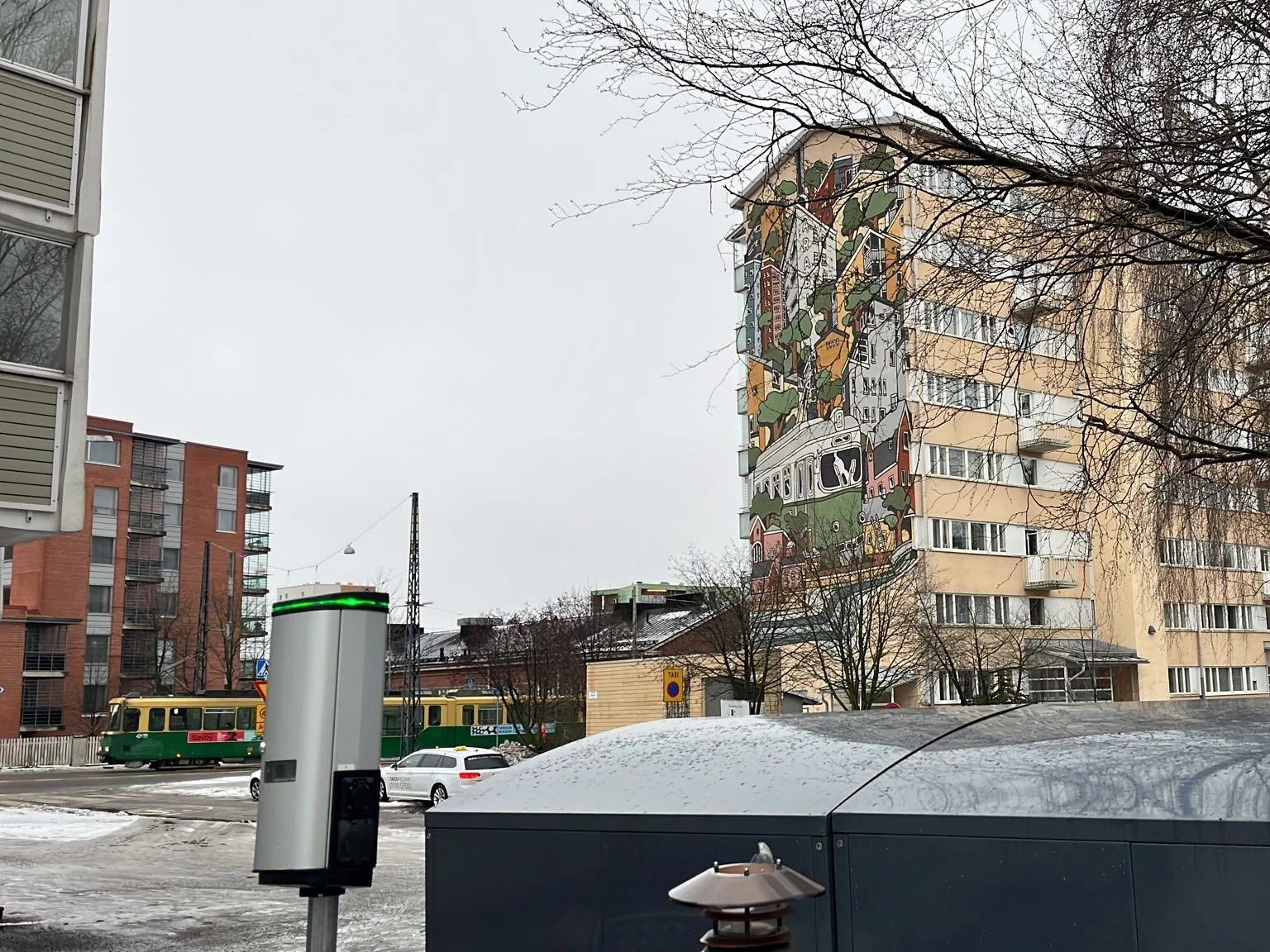 Picture from the city street, tall buildings, charger, gray sky and snow on the ground.