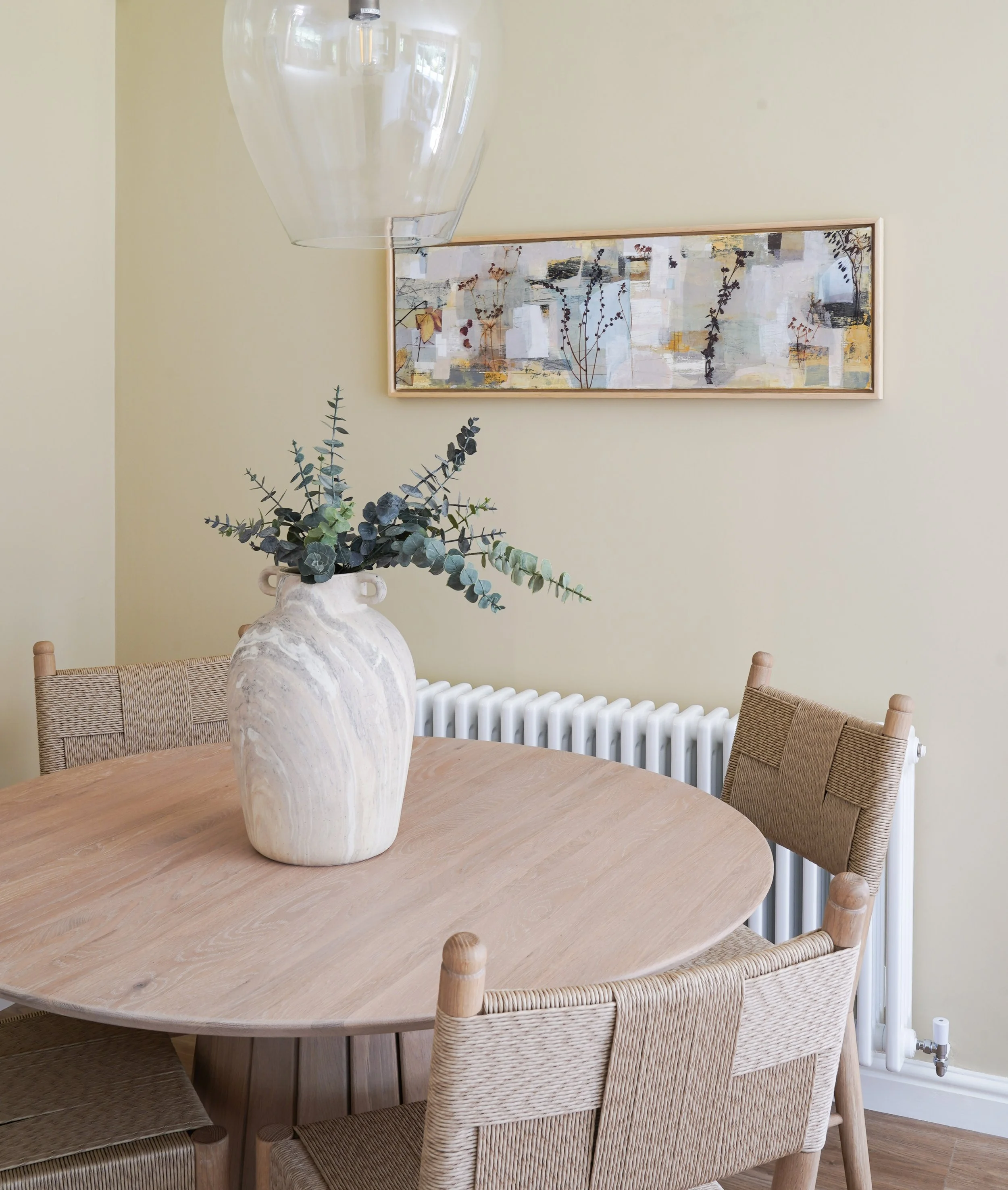 Neptune oak table and wicker chairs beneath sue johnsone artwork in a kitchen dining area