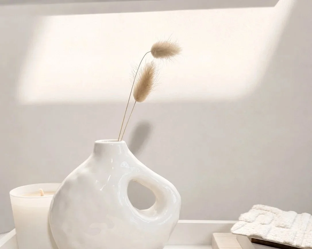 Light and shadow falling across a white vase and candle, showing how daylight changes white