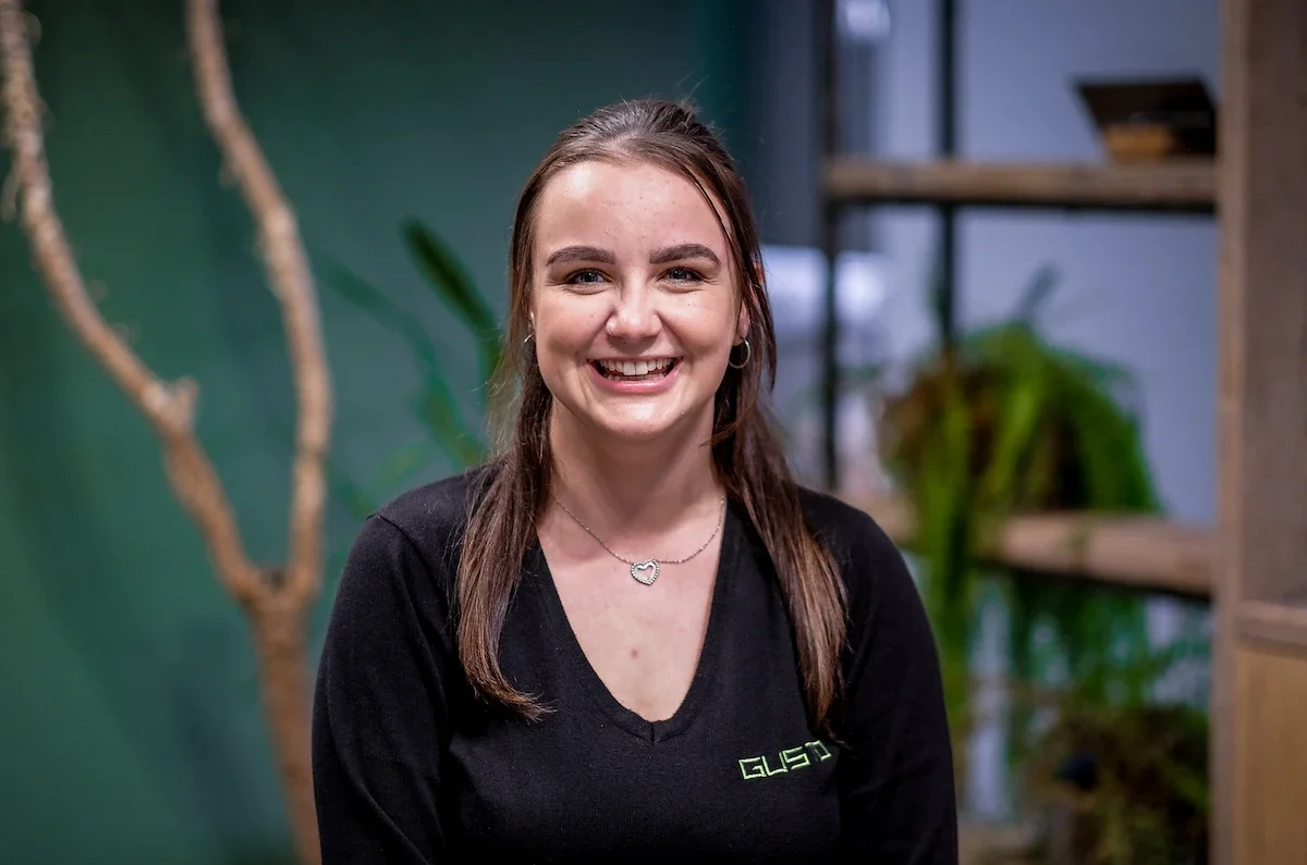 Young lady with straight dark hair smiling in front of a green background