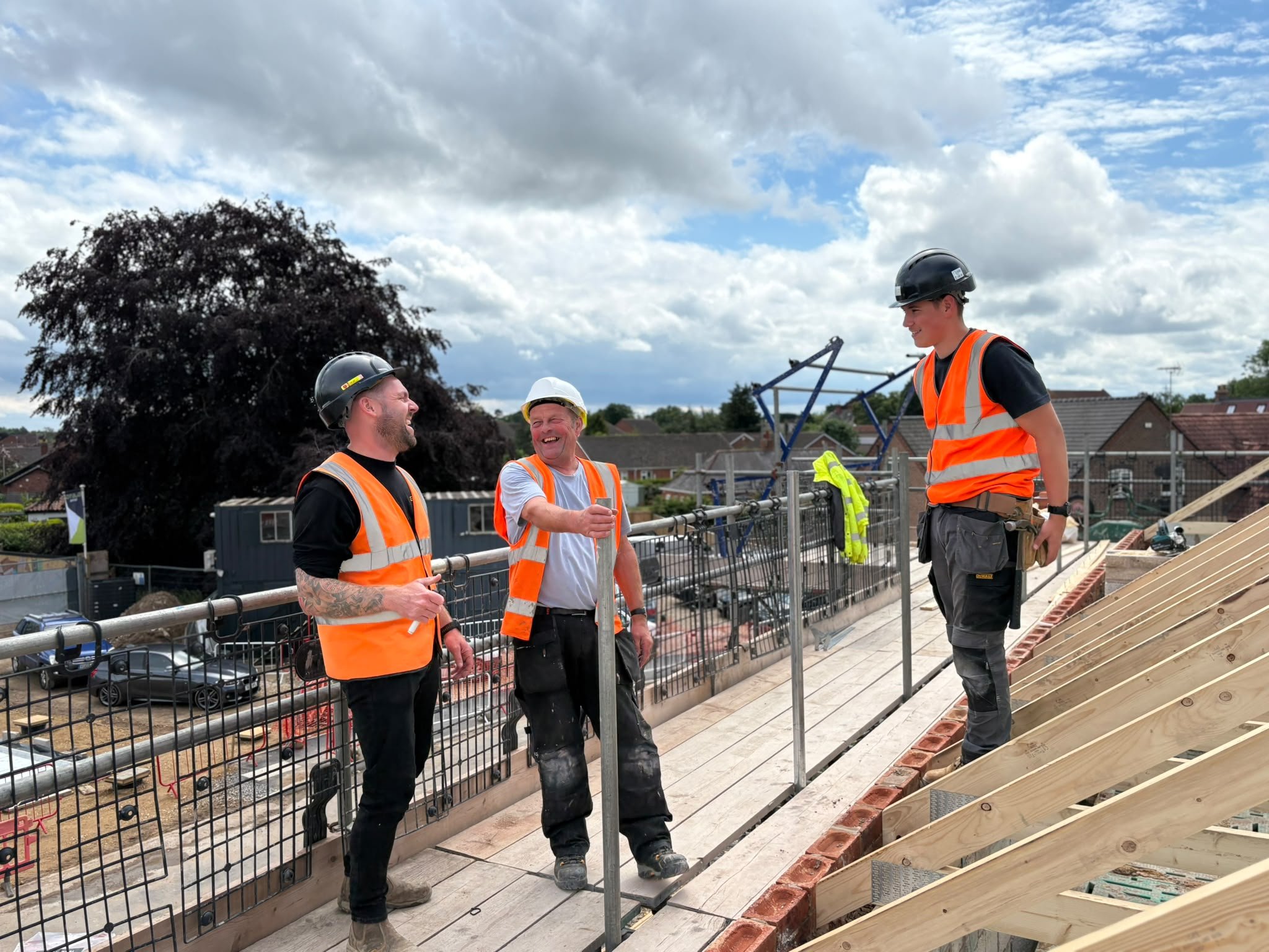 Three construction workers stood on a scaffold on site, blue sky and clouds