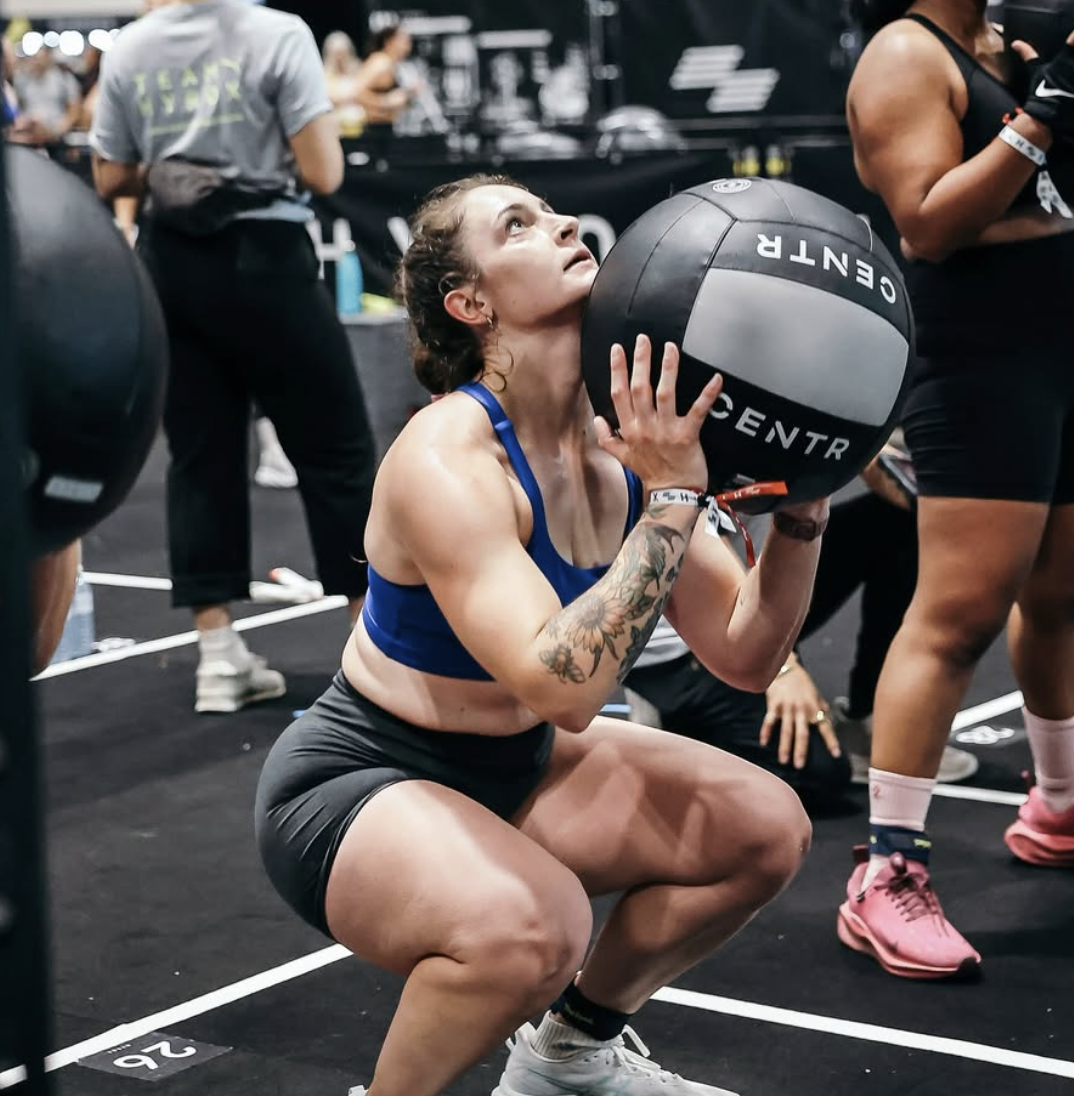 Woman in a gray sleeveless "Fit Collective St. Catharines" shirt smiling with arms crossed.