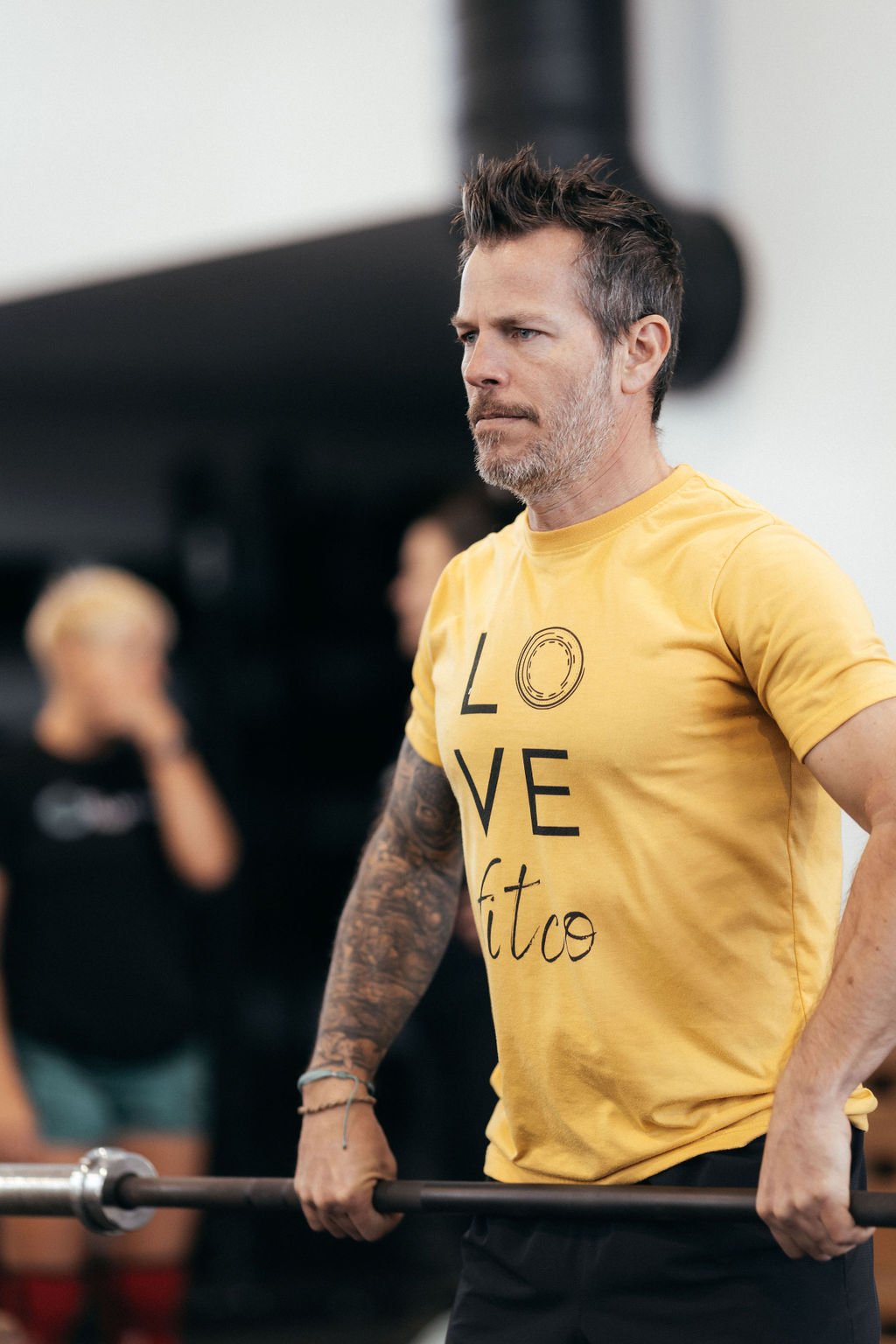 Person smiling, wearing a black "fit collection" t-shirt and a smartwatch, standing against a light background.