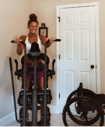 Brunette, smiling female in a front room wearing gym wear and using a standing frame.