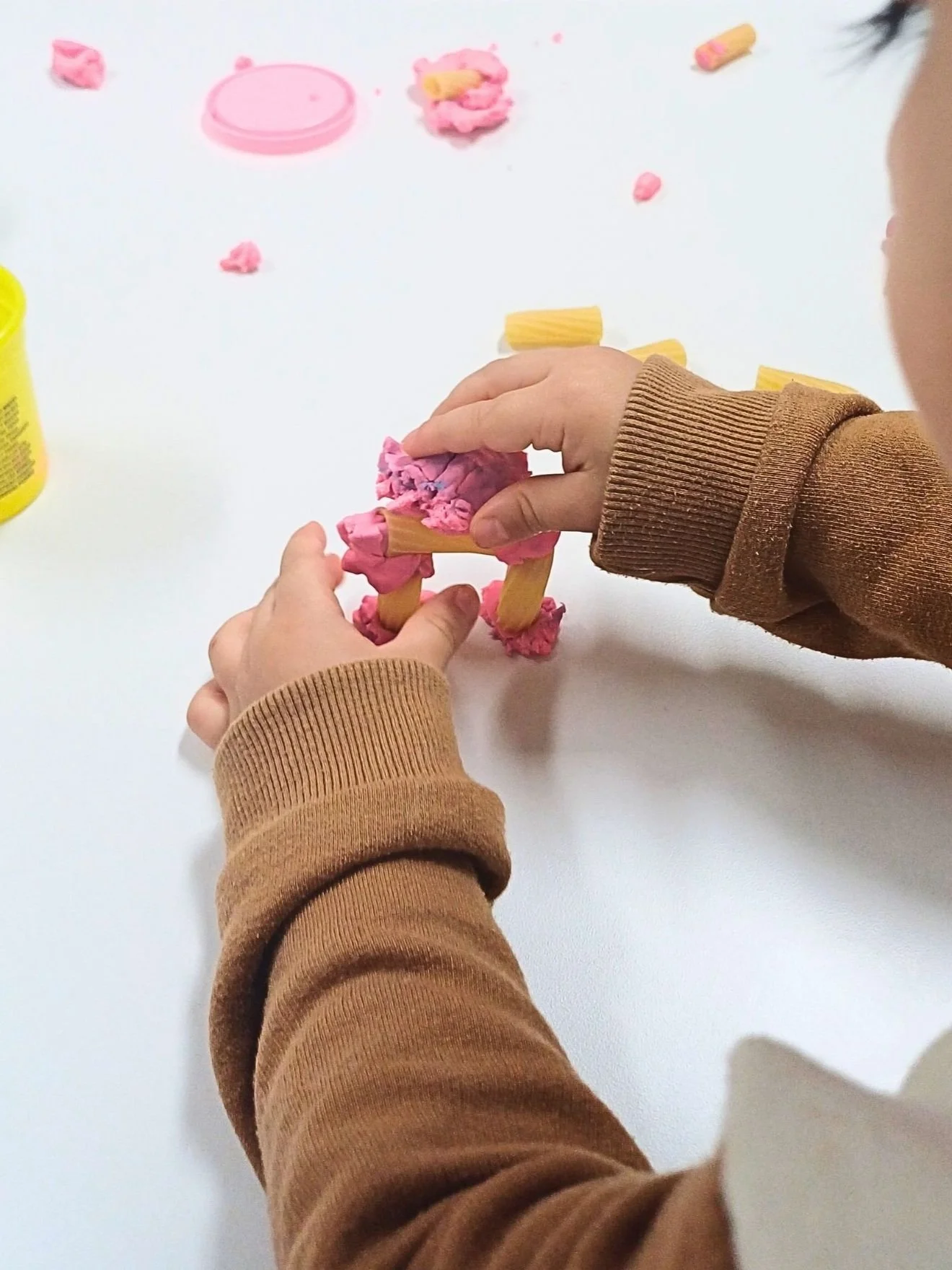 enfant construisant un pont avec de la pate a modeler et du rigatoni - objectif de construire un pont  avec differents outils a disposition pour favoriser la creativite et l esprit critique