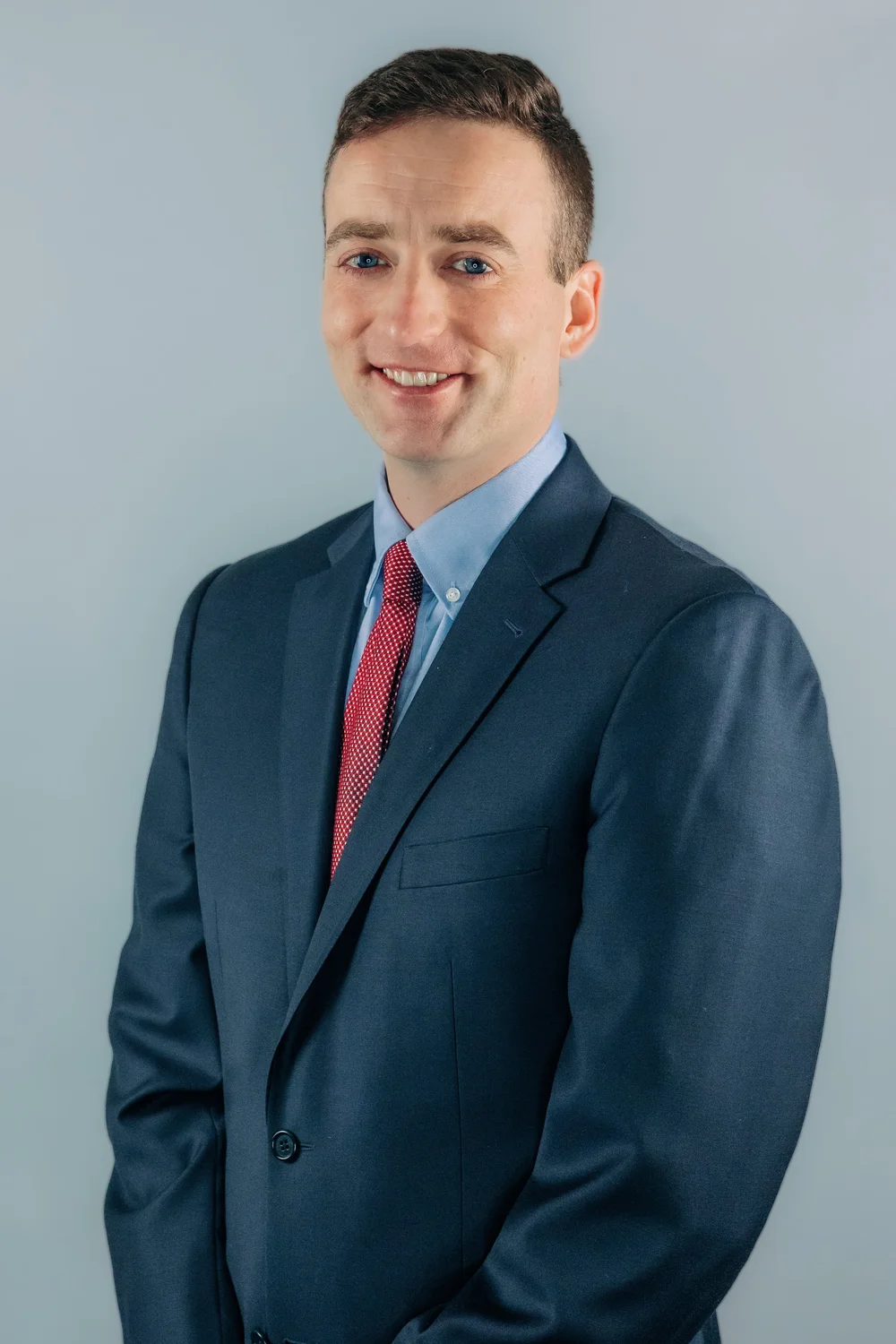 Professional headshot of attorney Scott Iseman smiling in a dark blue suit, light blue shirt, and red patterned tie against a light grey background.