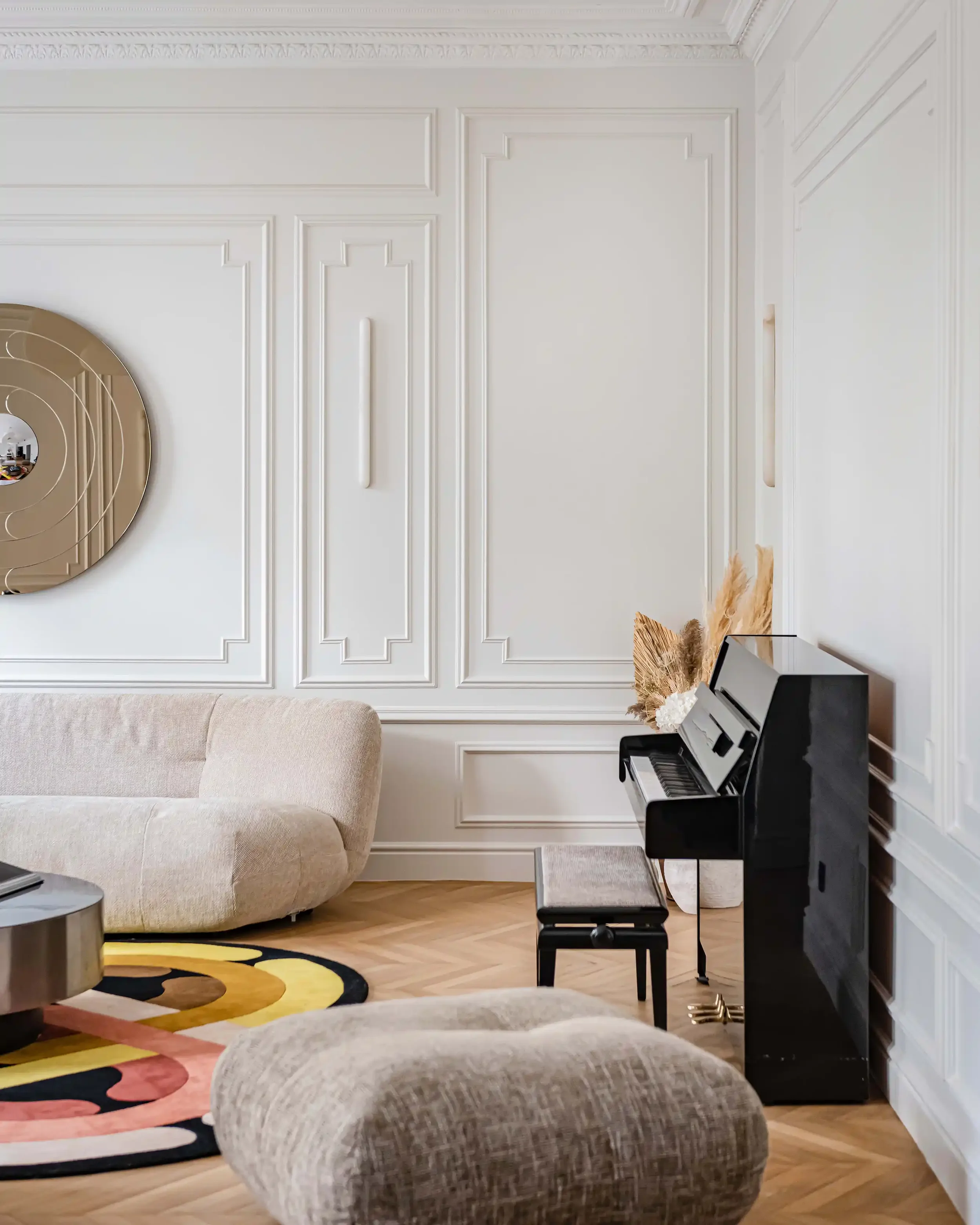 Détail d'un salon haussmannien haut de gamme avec piano droit noir, moulures murales classiques et parquet en point de Hongrie.