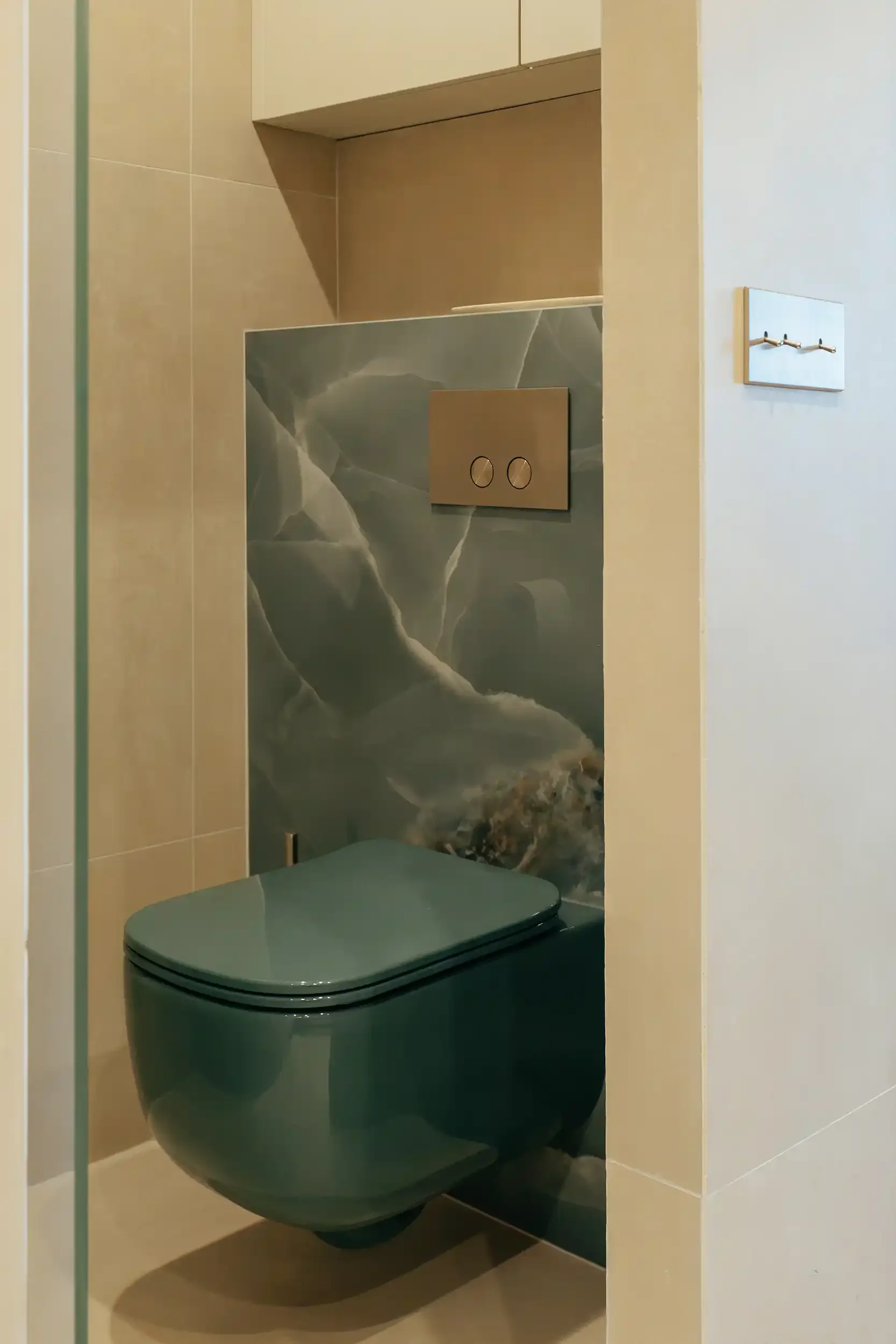 Toilettes modernes avec WC suspendu vert émeraude devant un panneau mural rétroéclairé en onyx bleu-vert.