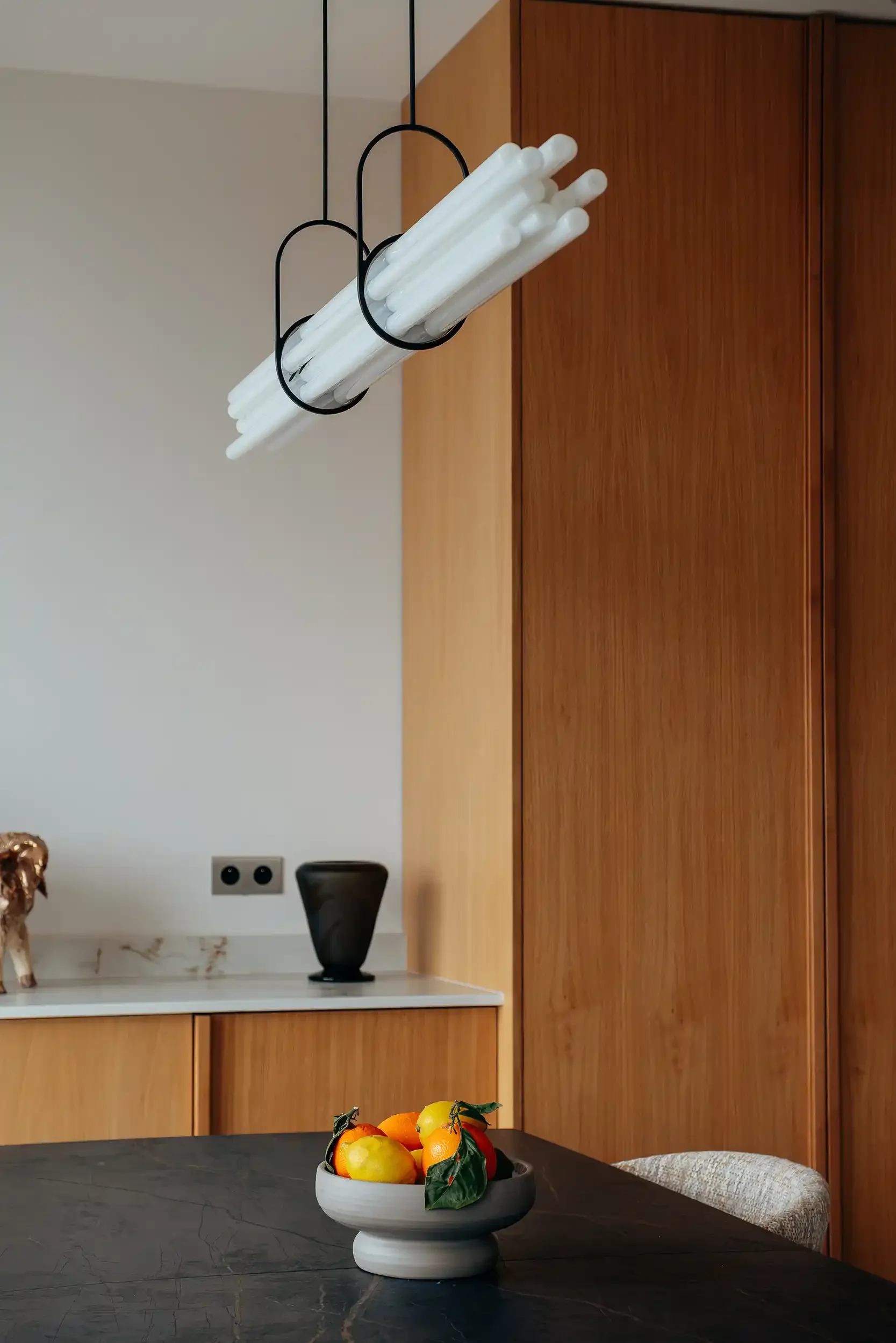 Zoom sur un luminaire suspendu contemporain au-dessus d'une table de salle à manger avec rangements en bois en arrière-plan.