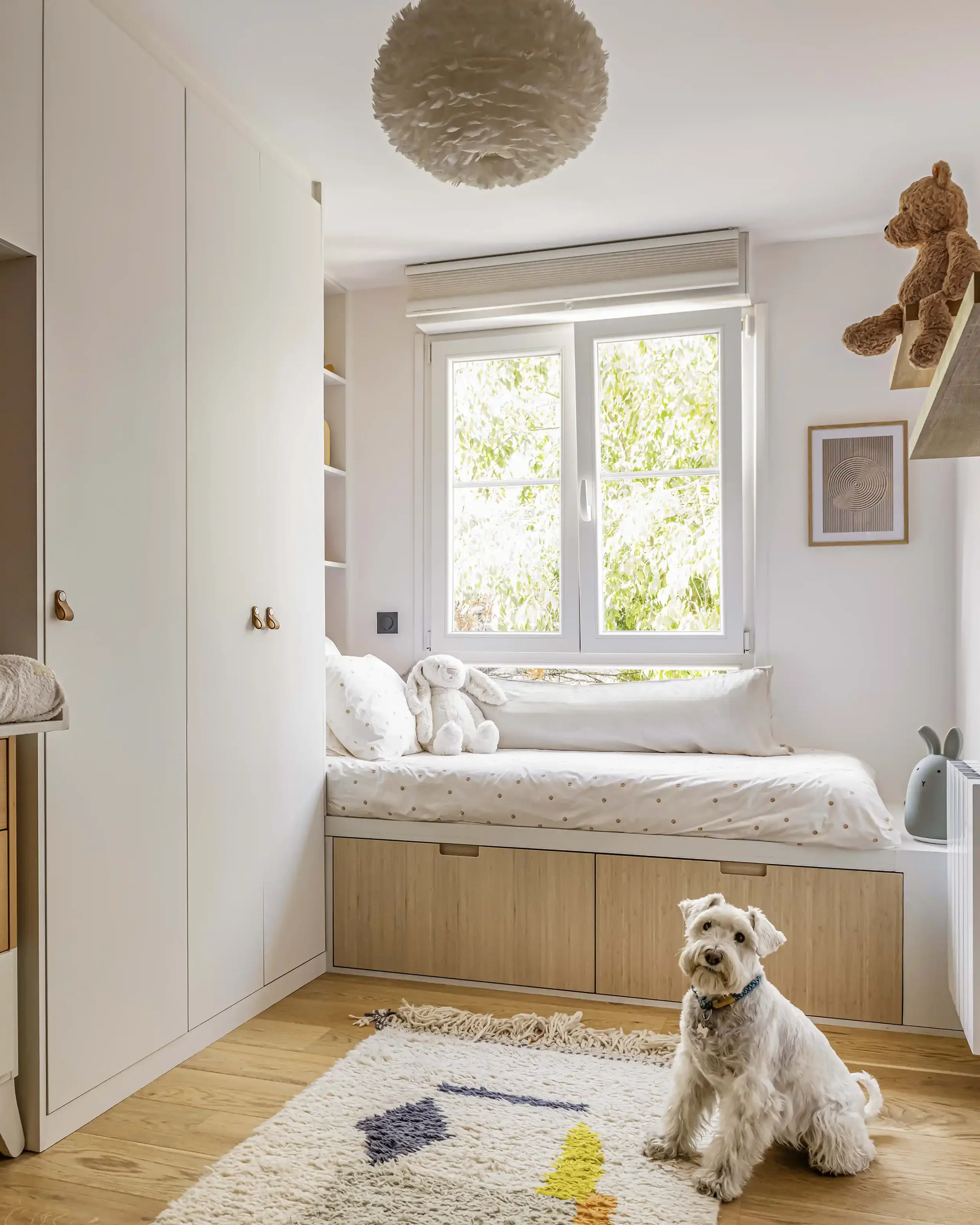 Chambre d'enfant lumineuse avec banquette de lecture sur mesure sous la fenêtre, rangements en chêne et parquet massif.