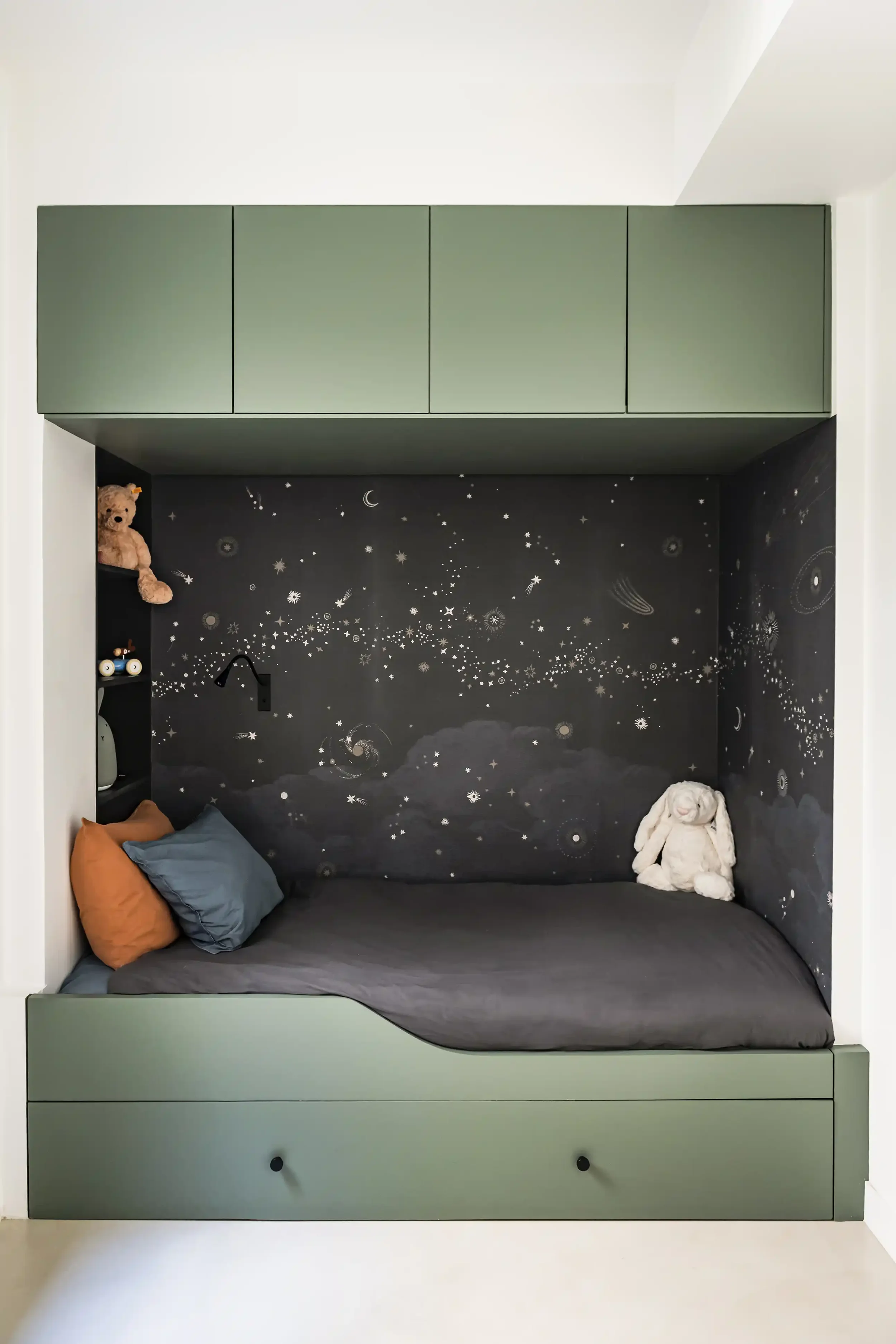 Aménagement de chambre enfant avec niche lit et chevet intégrée dans un meuble sur-mesure et tapisserie décorative.