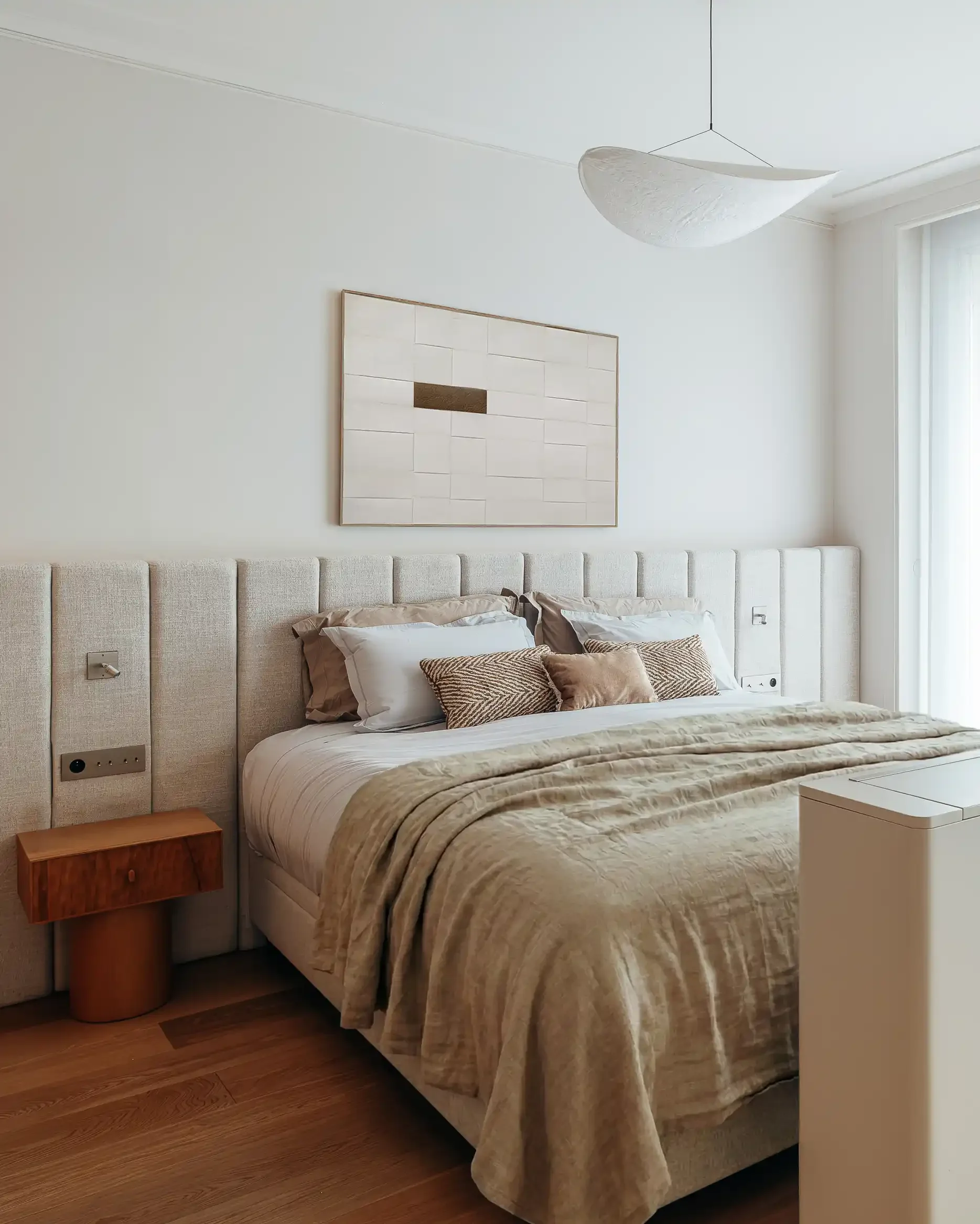 Suite parentale élégante avec tête de lit monumentale en tissu à panneaux verticaux et table de nuit en bois clair.