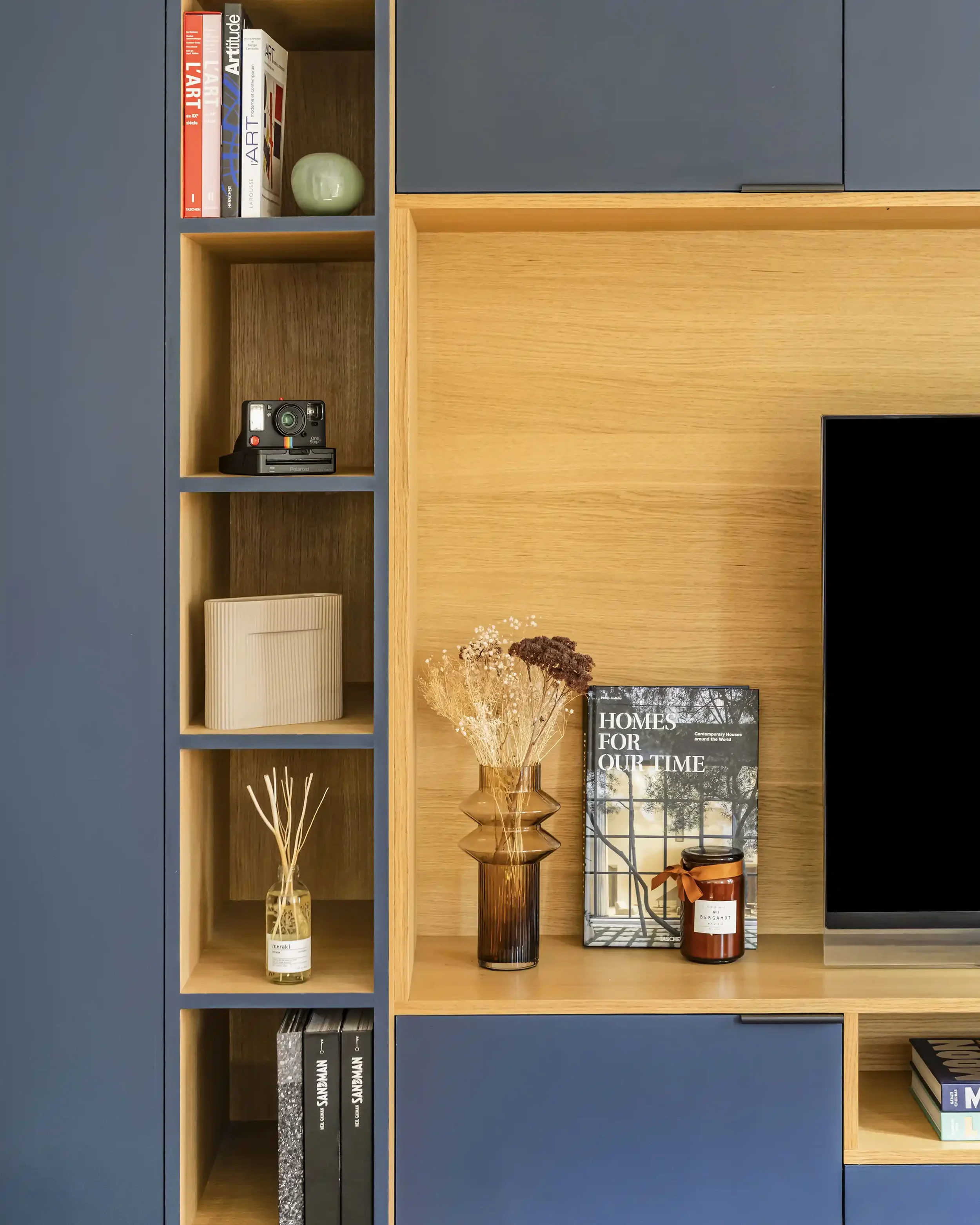 Détail d'une bibliothèque sur mesure alliant façades bleu nuit et niches en bois avec objets de décoration.