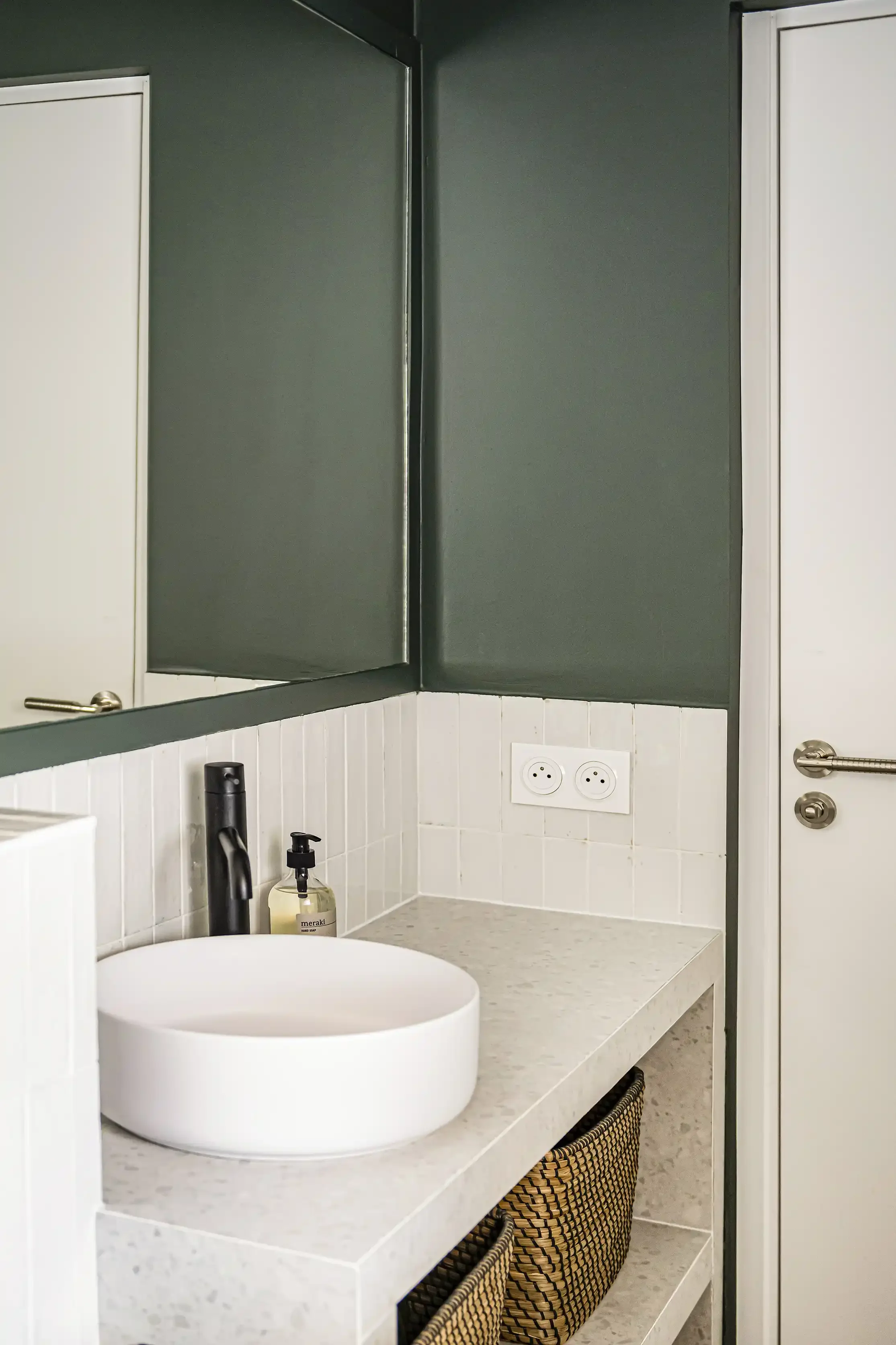 Salle de bain élégante avec meuble vasque en terrazzo, murs vert sapin et miroir rond.