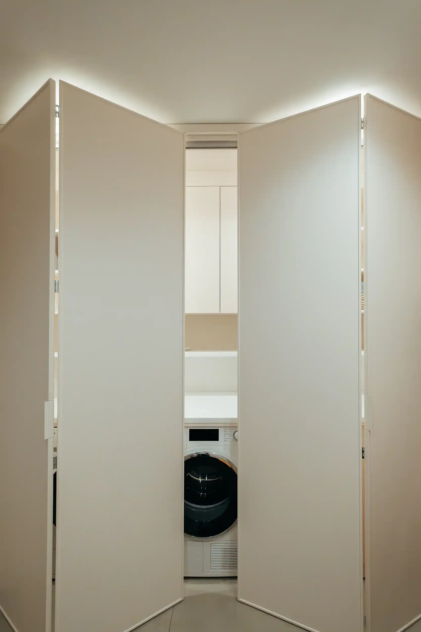 Placard de buanderie sur mesure avec portes pliantes blanches rétroéclairées dissimulant un lave-linge séchant.