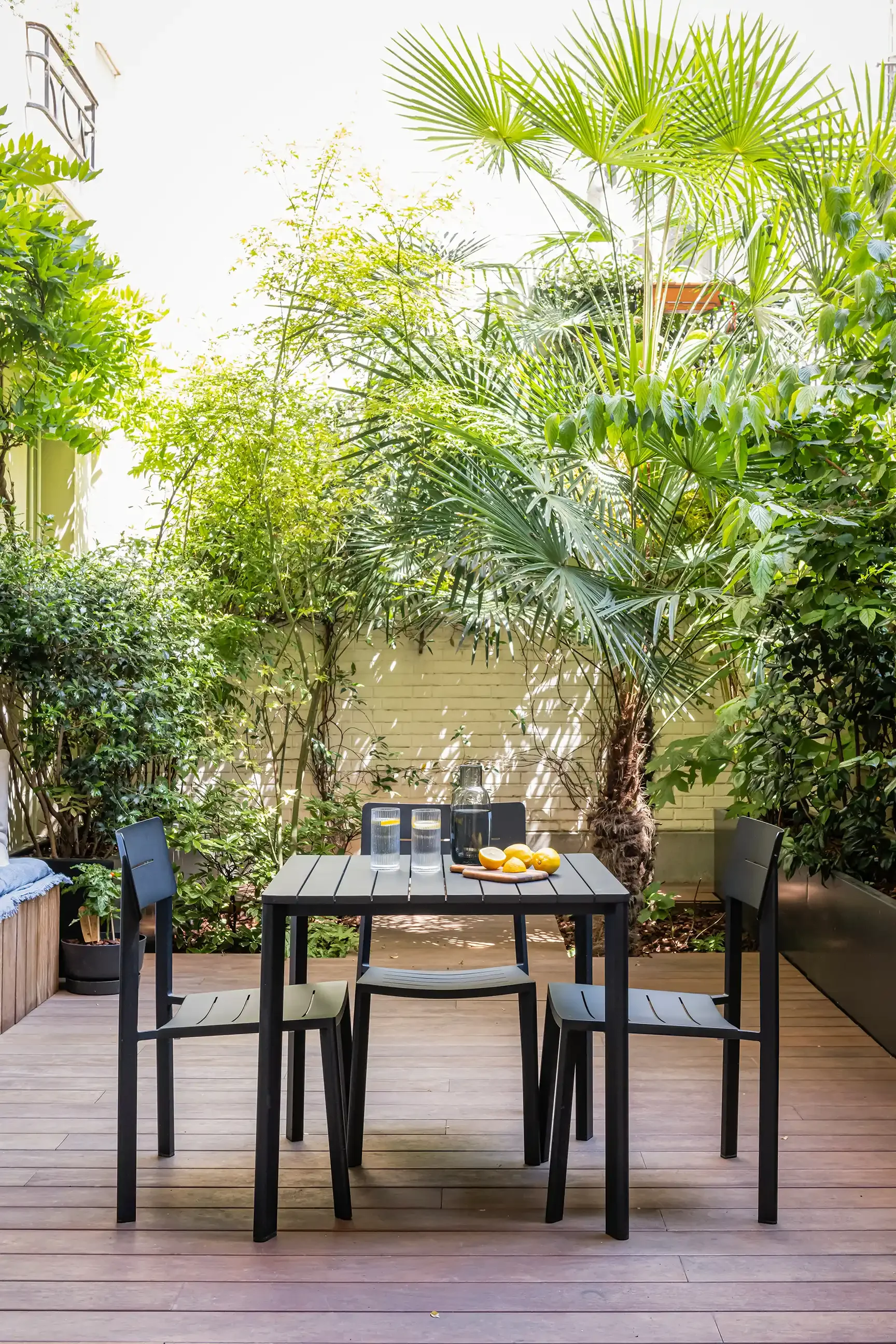 Aménagement d'une terrasse urbaine avec revêtement en bois, table de jardin noire moderne et grands palmiers exotiques en arrière-plan.