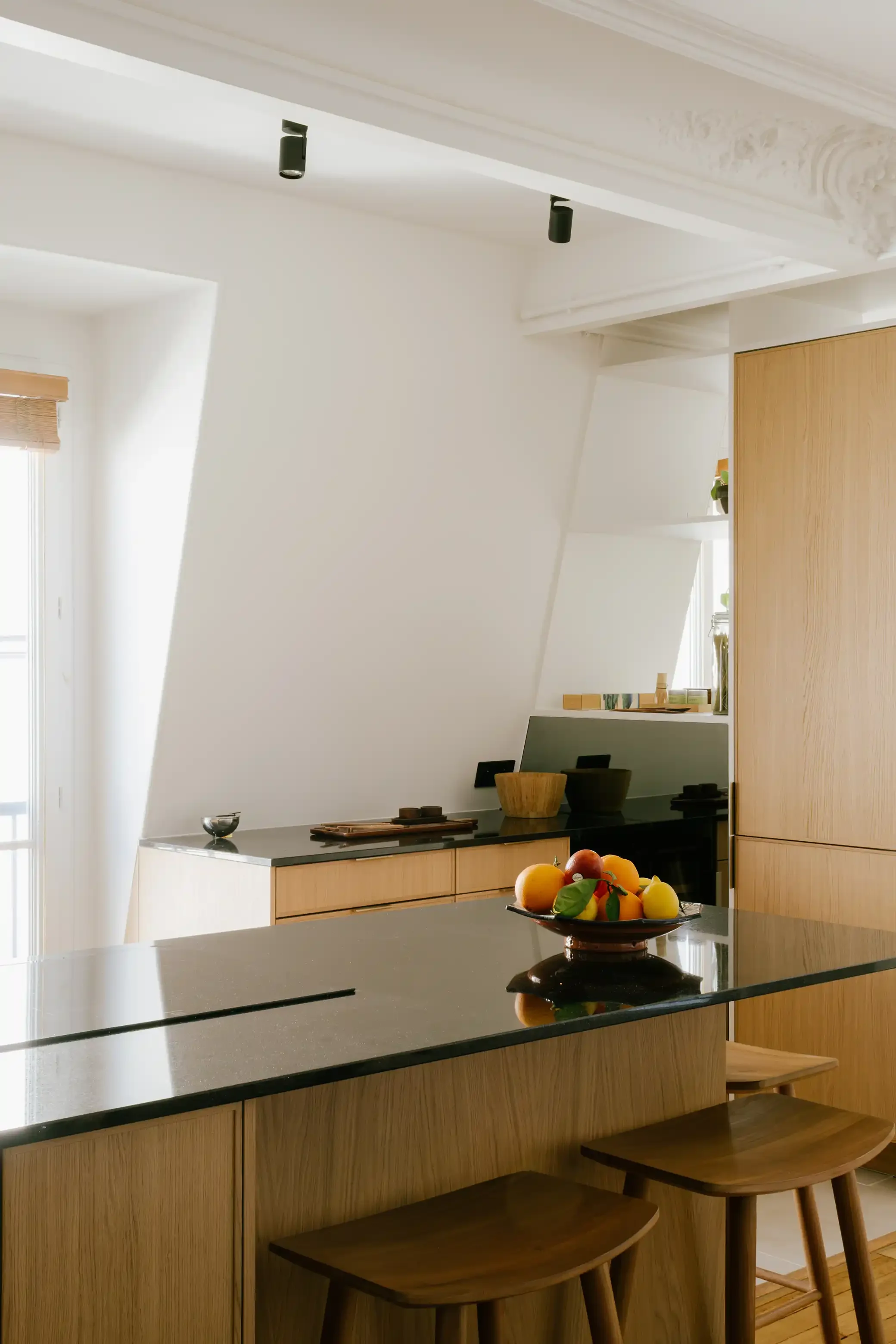 Îlot central de cuisine en bois avec évier intégré et plan de travail en granit noir, décoration minimaliste dans un appartement à Paris.