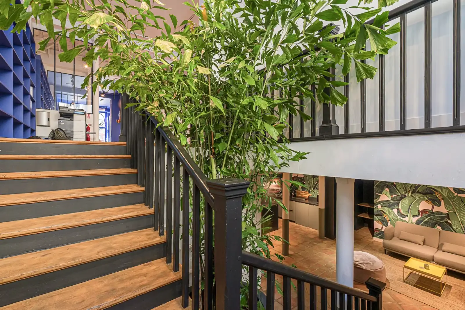 Escalier moderne en bois et métal noir dans une agence immobilière parisienne avec vue sur un espace lounge végétalisé.