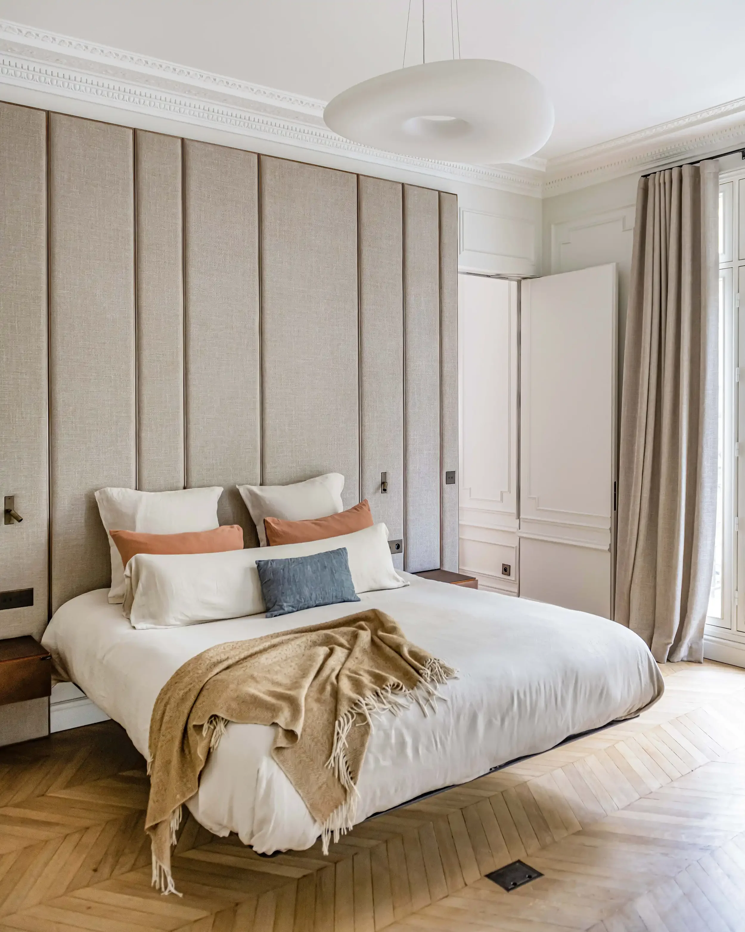 Suite parentale de luxe avec tête de lit en tissu et laiton, parquet en point de Hongrie et moulures au plafond.