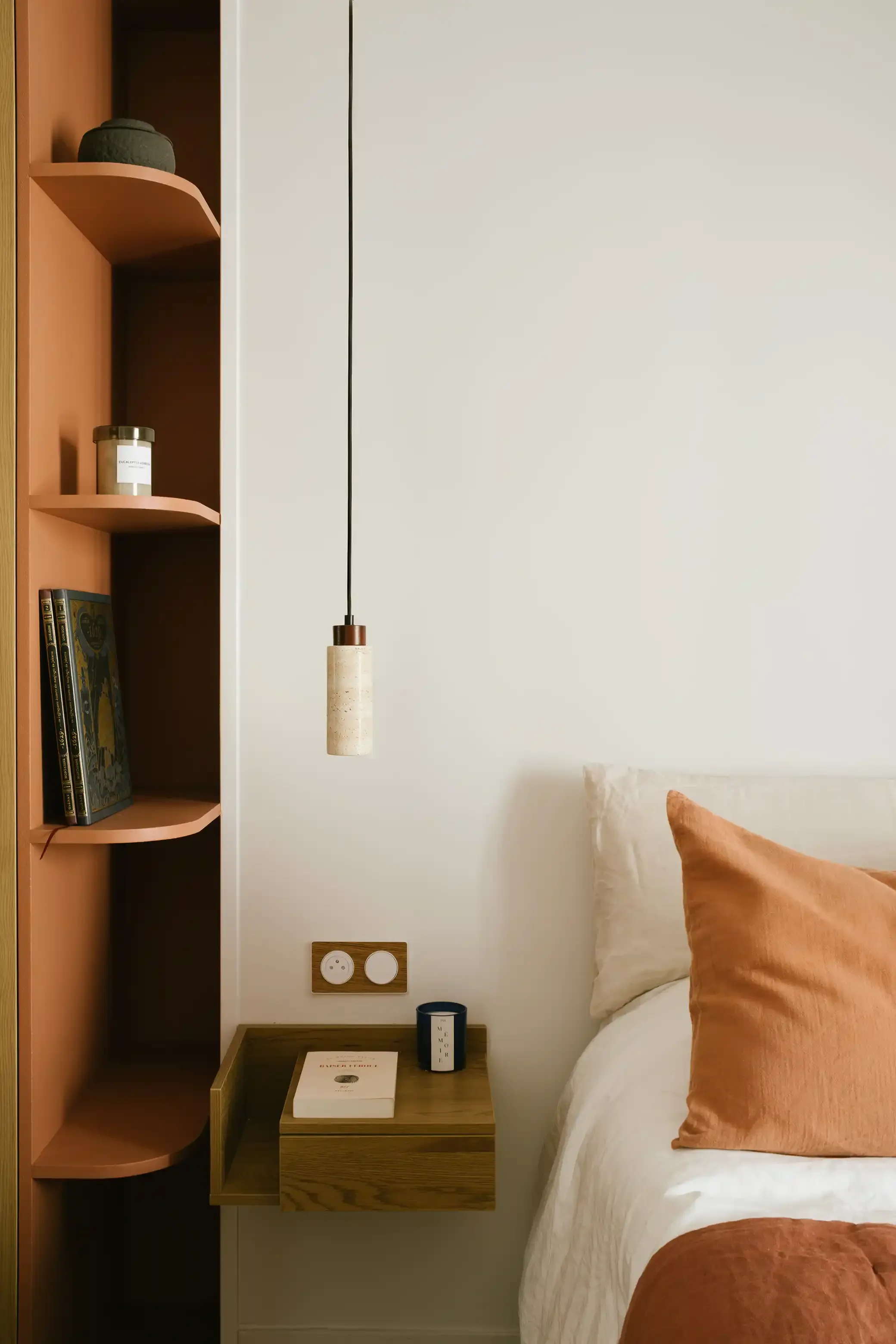 Coin nuit avec table de chevet suspendue en bois, niche de rangement terracotta et luminaire moderne en travertin.