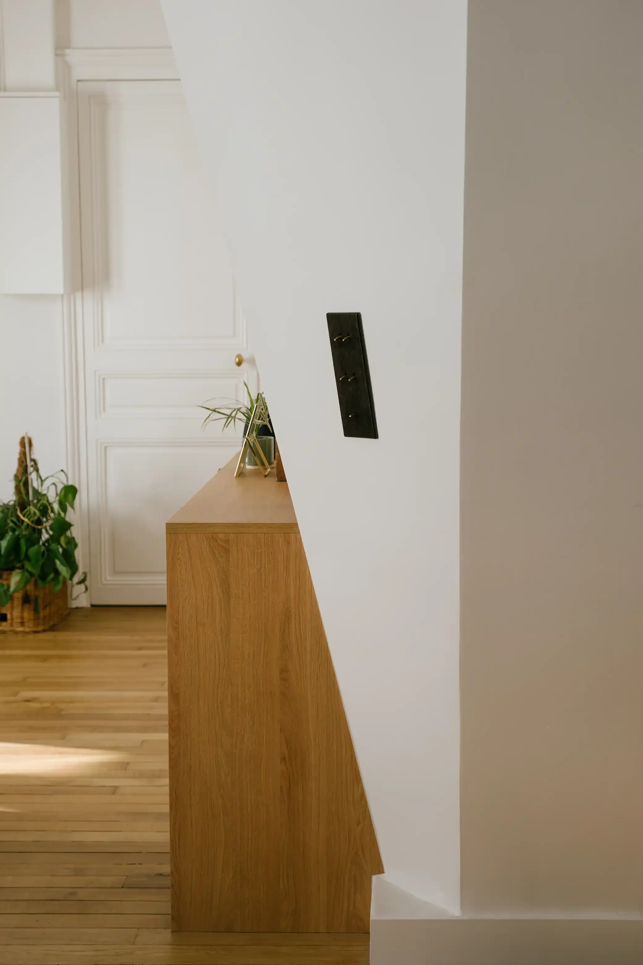 Détail d'un interrupteur vintage en laiton noir à leviers installé sur une cloison blanche avec vue sur un parquet ancien et des moulures.