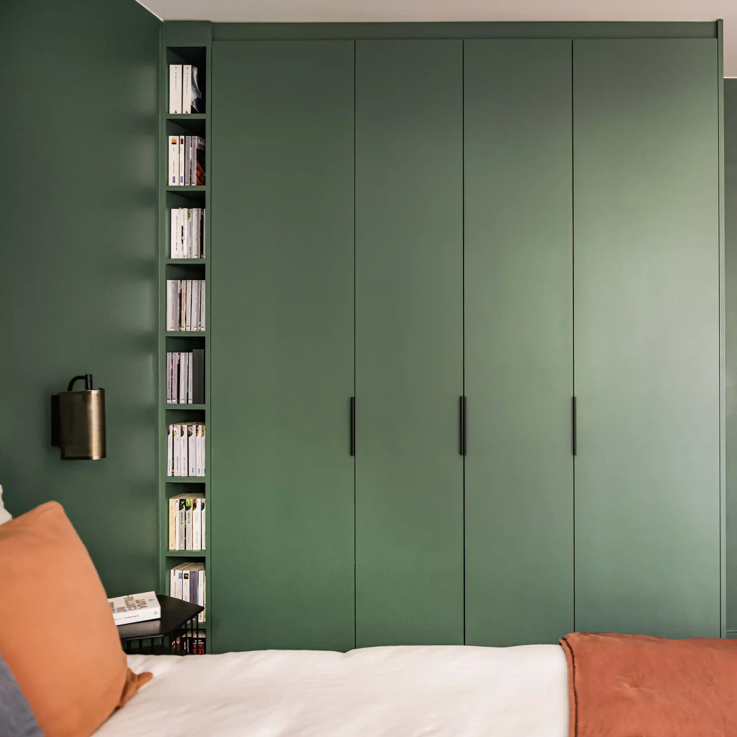 Dressing sur mesure vert forêt toute hauteur avec colonne de rangement pour livres intégrée et poignées noires minimalistes.
