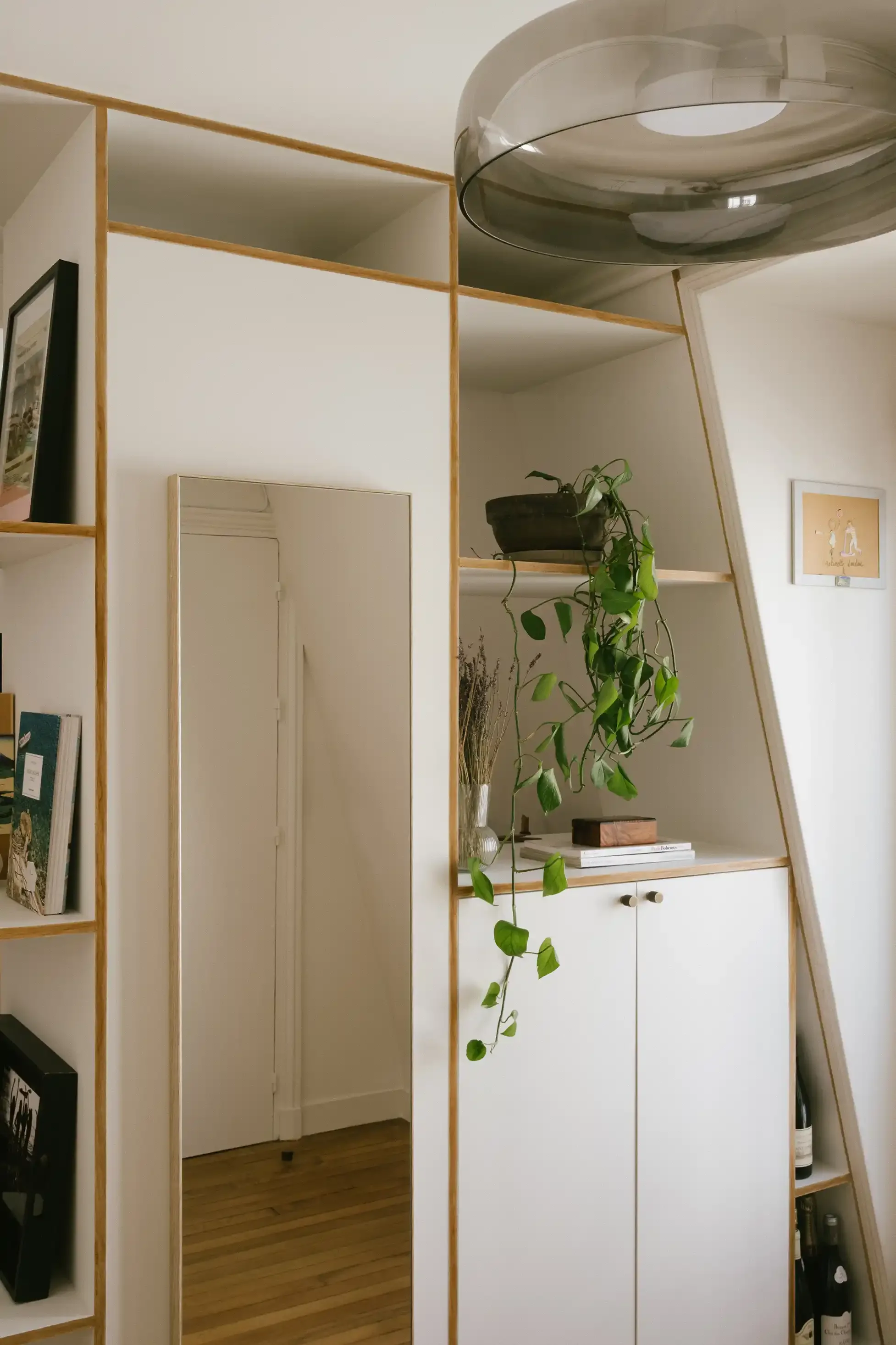 Bibliothèque blanche sur-mesure épousant la pente du toit avec étagères ouvertes, placards bas et miroir intégré pour optimiser l'espace.