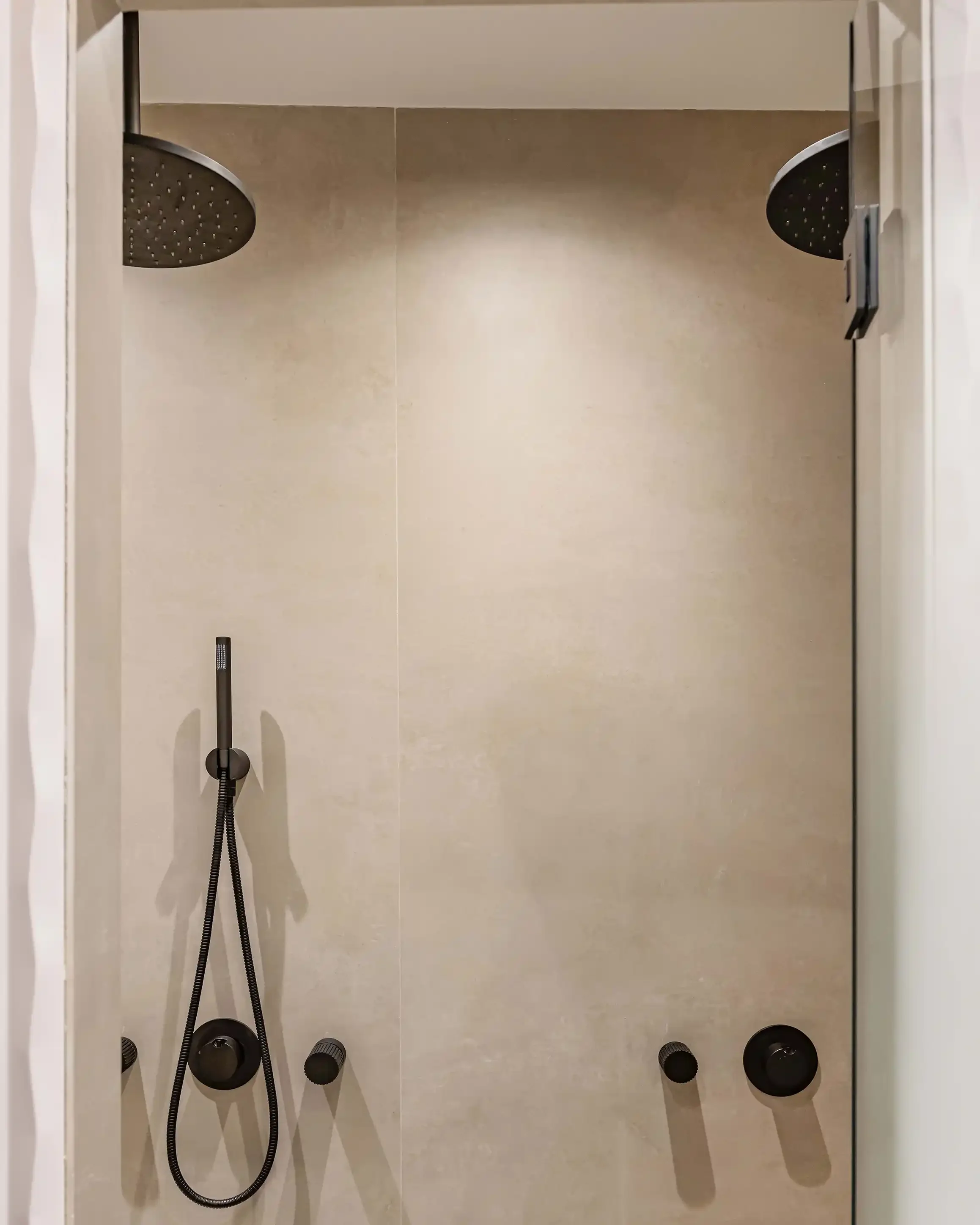 Grande douche à l'italienne double avec robinetterie noire mate encastrée, parois en pierre naturelle et receveur minimaliste.