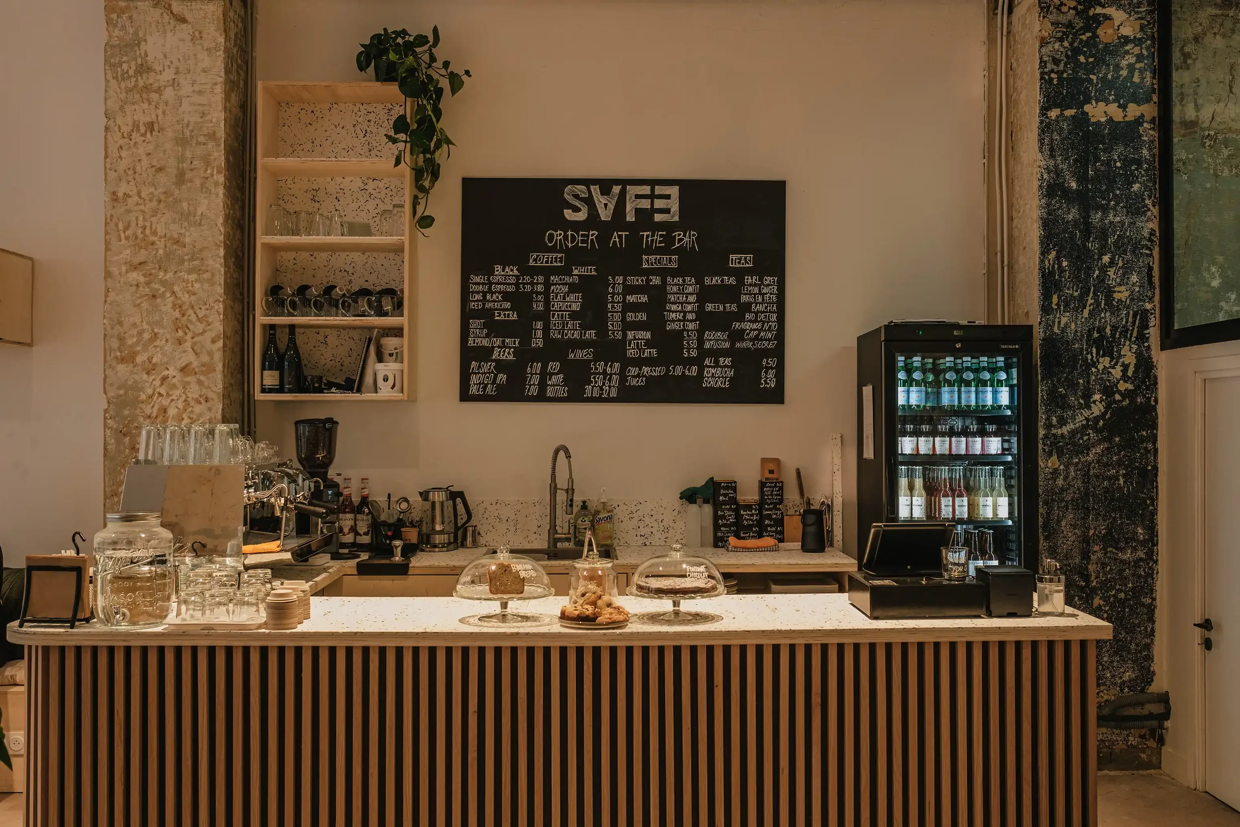 Comptoir en bois et marbre d'un café de spécialité à Paris avec menu à la craie, pâtisseries artisanales et machine à espresso professionnelle.