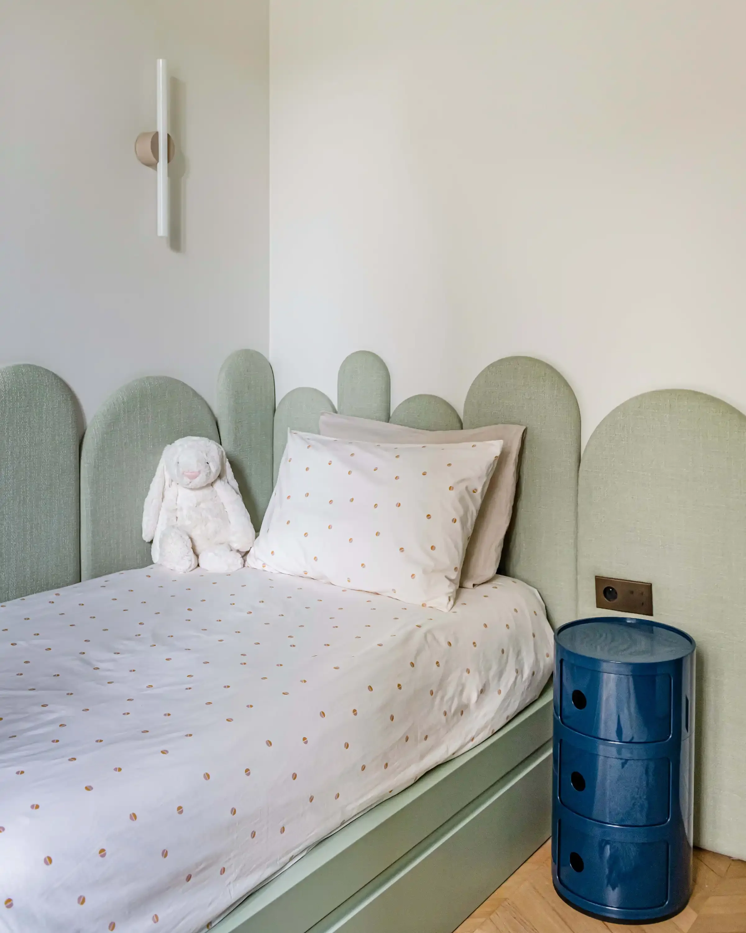 Détail d'une chambre d'enfant avec tête de lit sur mesure en forme de nuage et menuiserie vert amande.