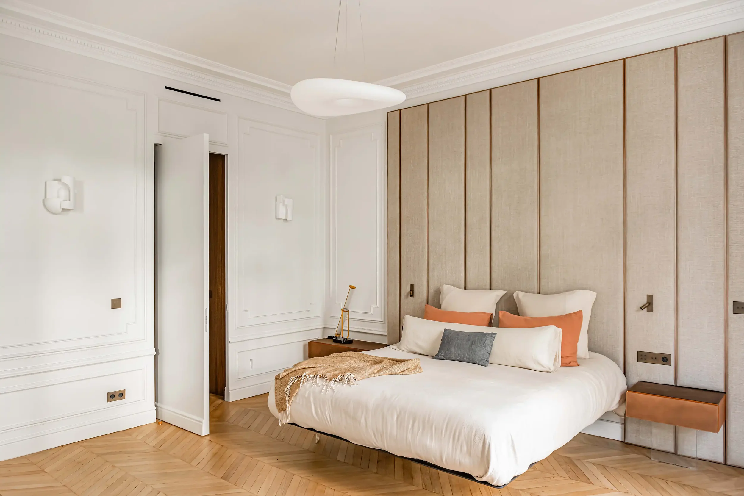 Suite parentale élégante avec lit suspendu, tête de lit monumentale en textile et architecture haussmannienne.