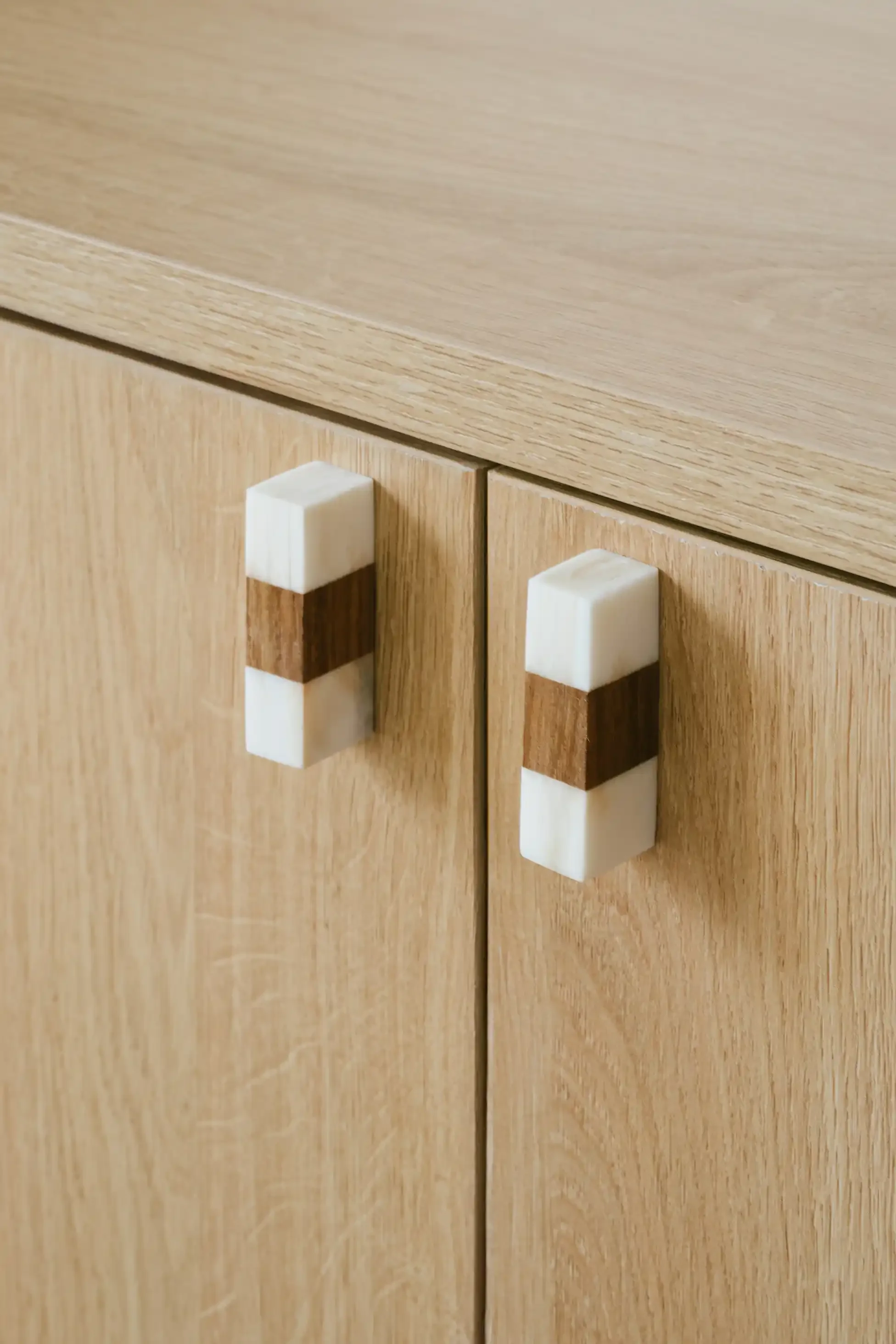 Détail de poignées de meubles artisanales en marbre blanc et bois sur des façades de placards en chêne clair.