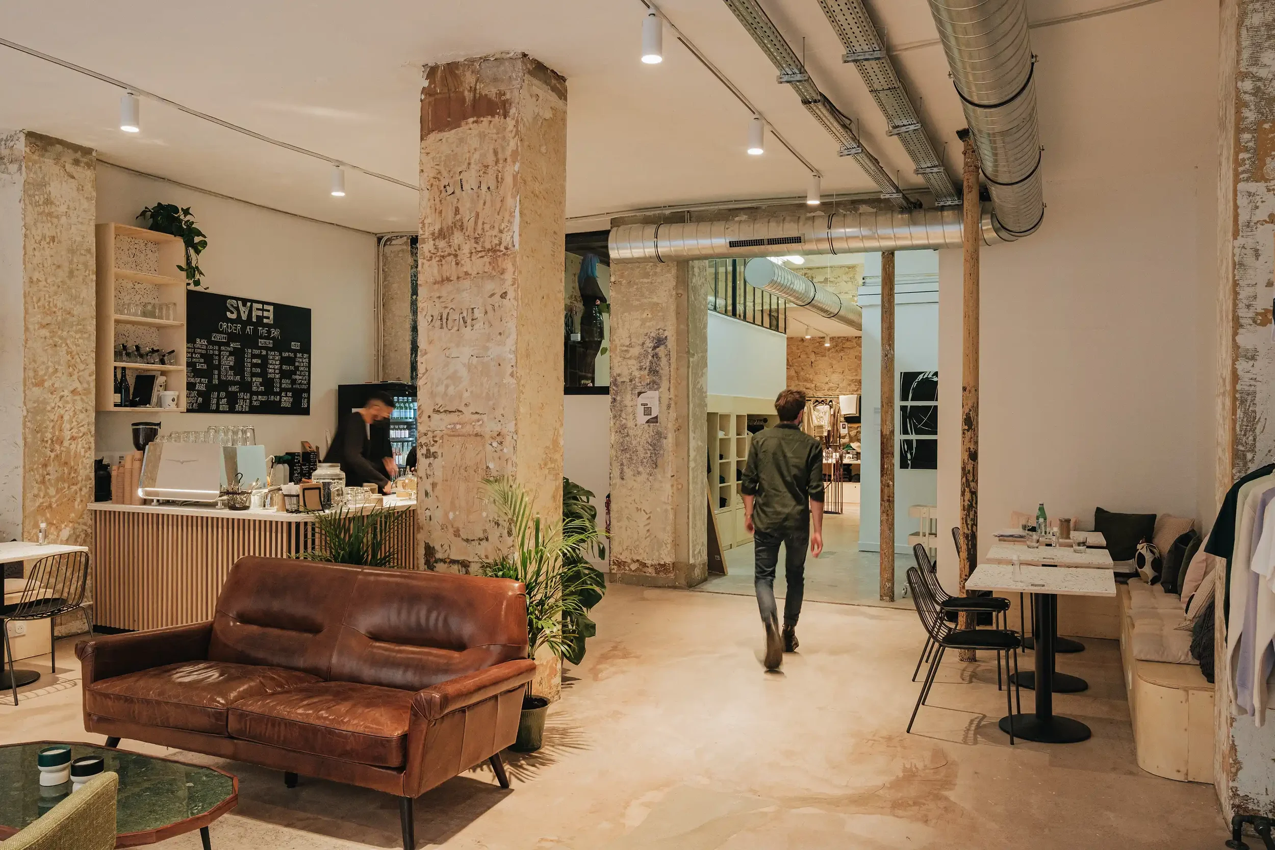 Ambiance d'un lieu de vie hybride à Paris mêlant coffee shop, boutique de mode éthique et espace de travail partagé avec murs en pierre.