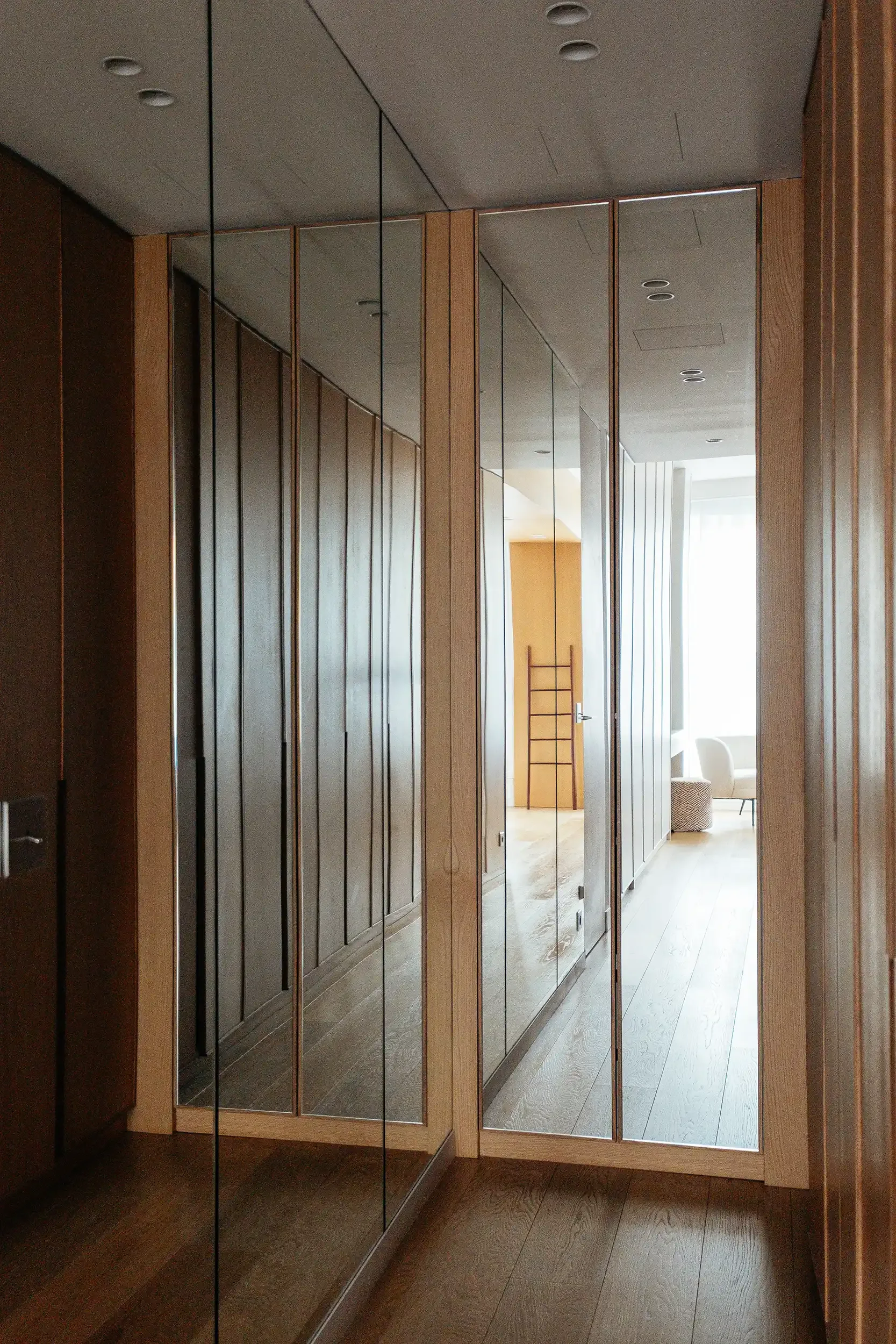 Couloir d'entrée étroit optimisé par de grands panneaux de miroirs muraux et des placards intégrés en bois de chêne.