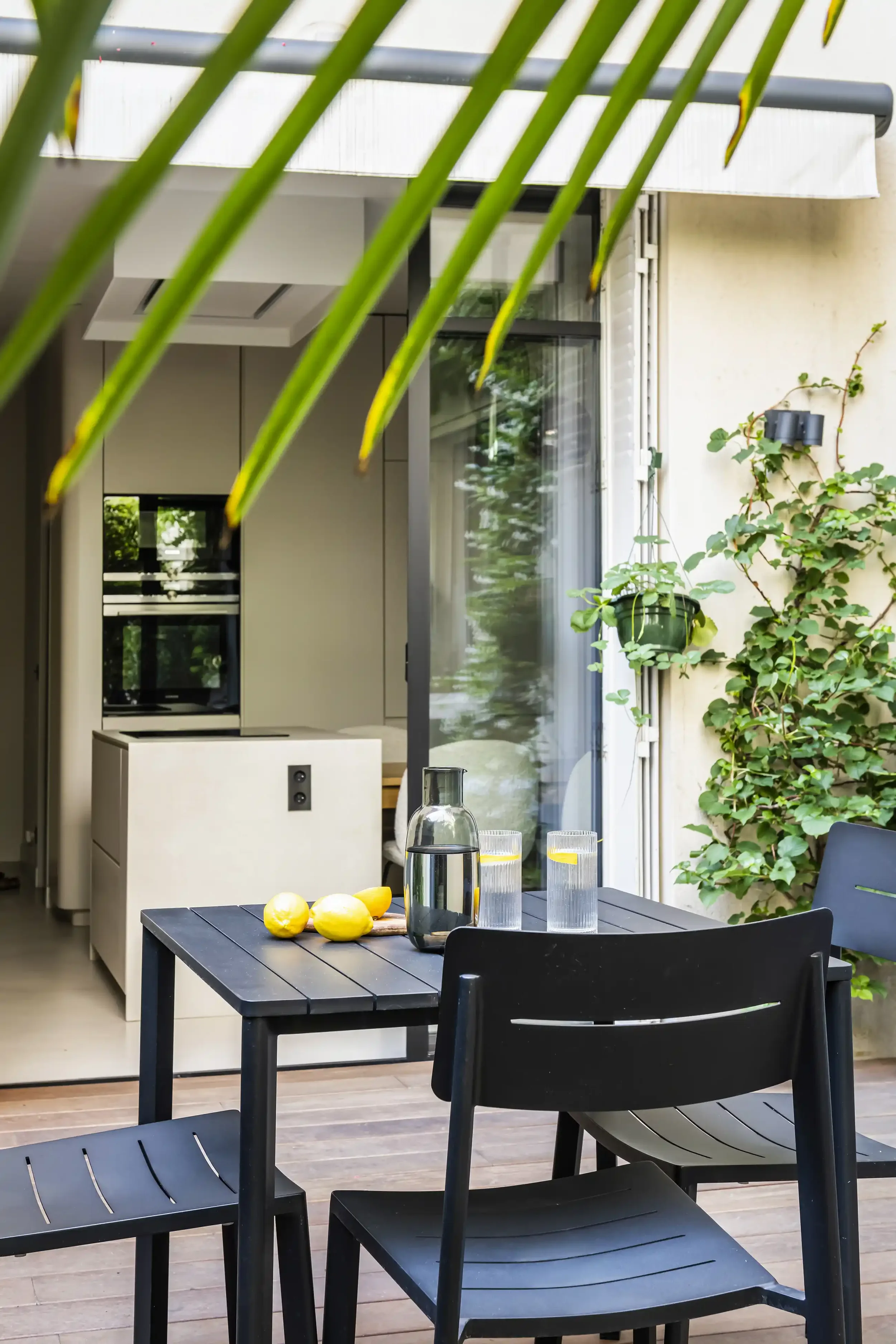 Espace repas extérieur sur une terrasse en bois avec vue sur l'îlot central d'une cuisine moderne ouverte.