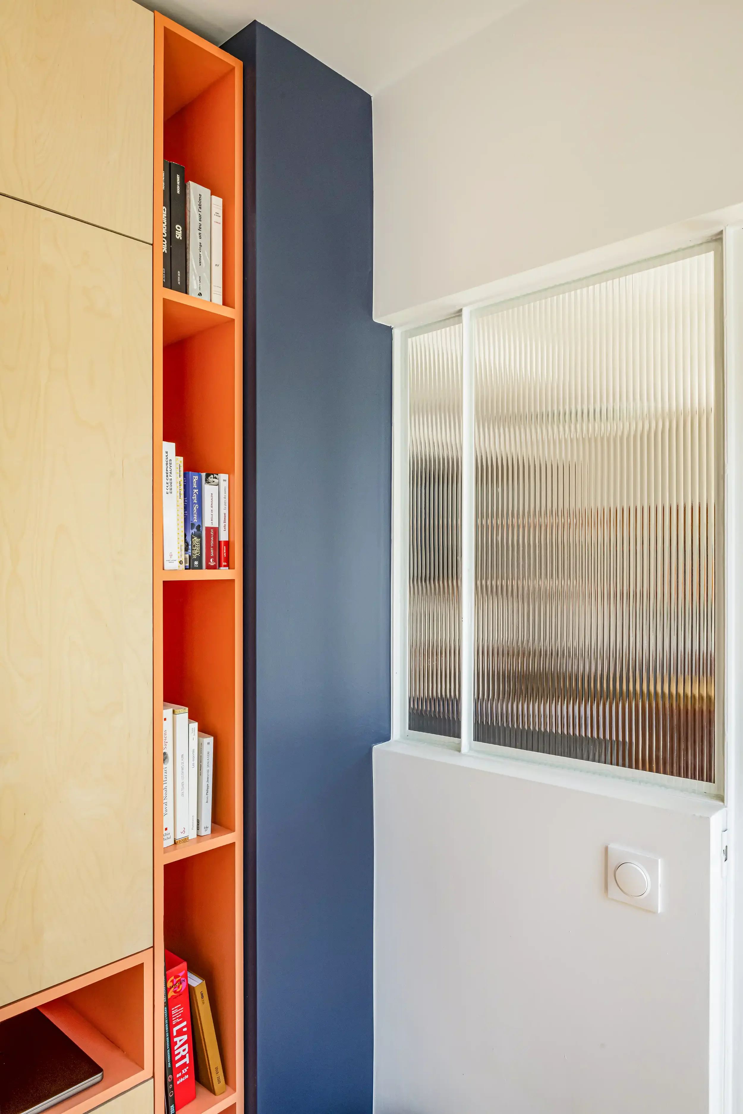 Bibliothèque sur mesure orange vif au design contemporain avec niches de rangement ouvertes et fermées.