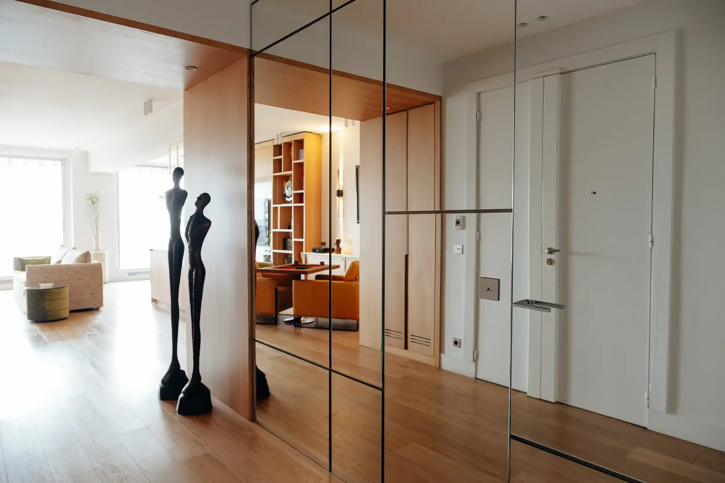 Entrée d'appartement prestigieux avec grand miroir fumé à partitions métalliques et sculptures longilignes en bronze.
