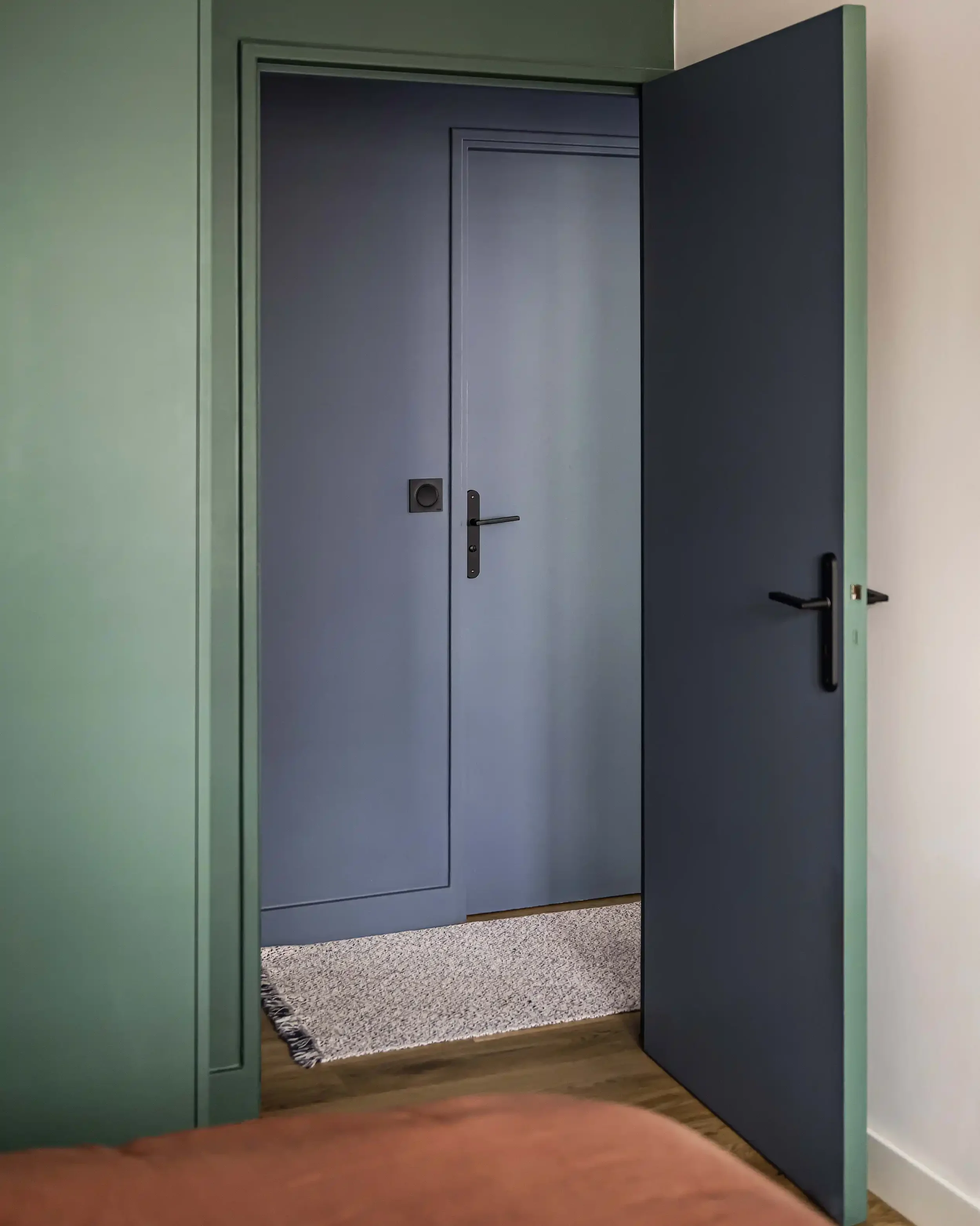 Porte intérieure peinte en bleu nuit créant un contraste moderne avec les murs verts de l'appartement.